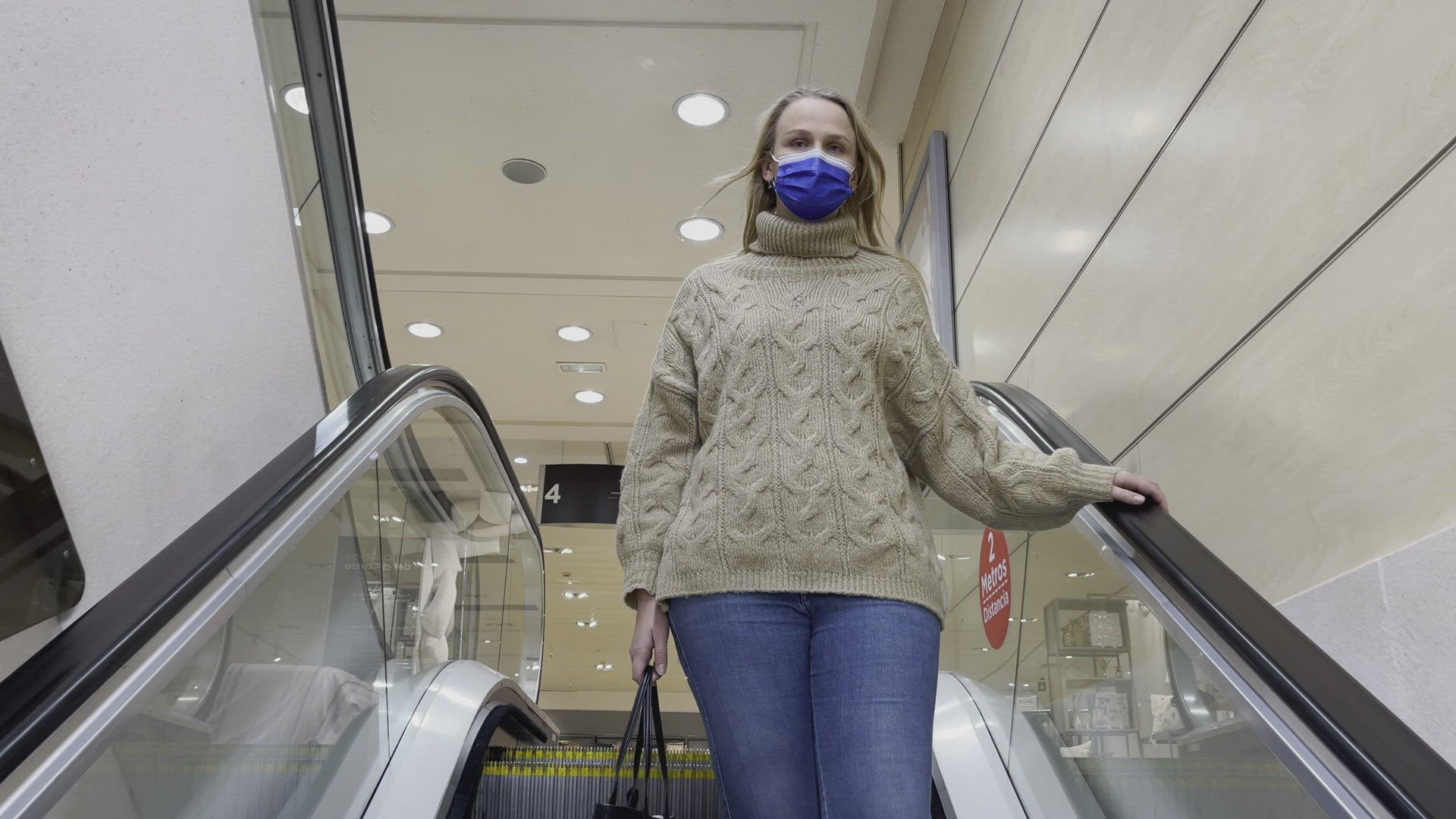 Woman in medical mask getting downstairs by escalator in trade centre