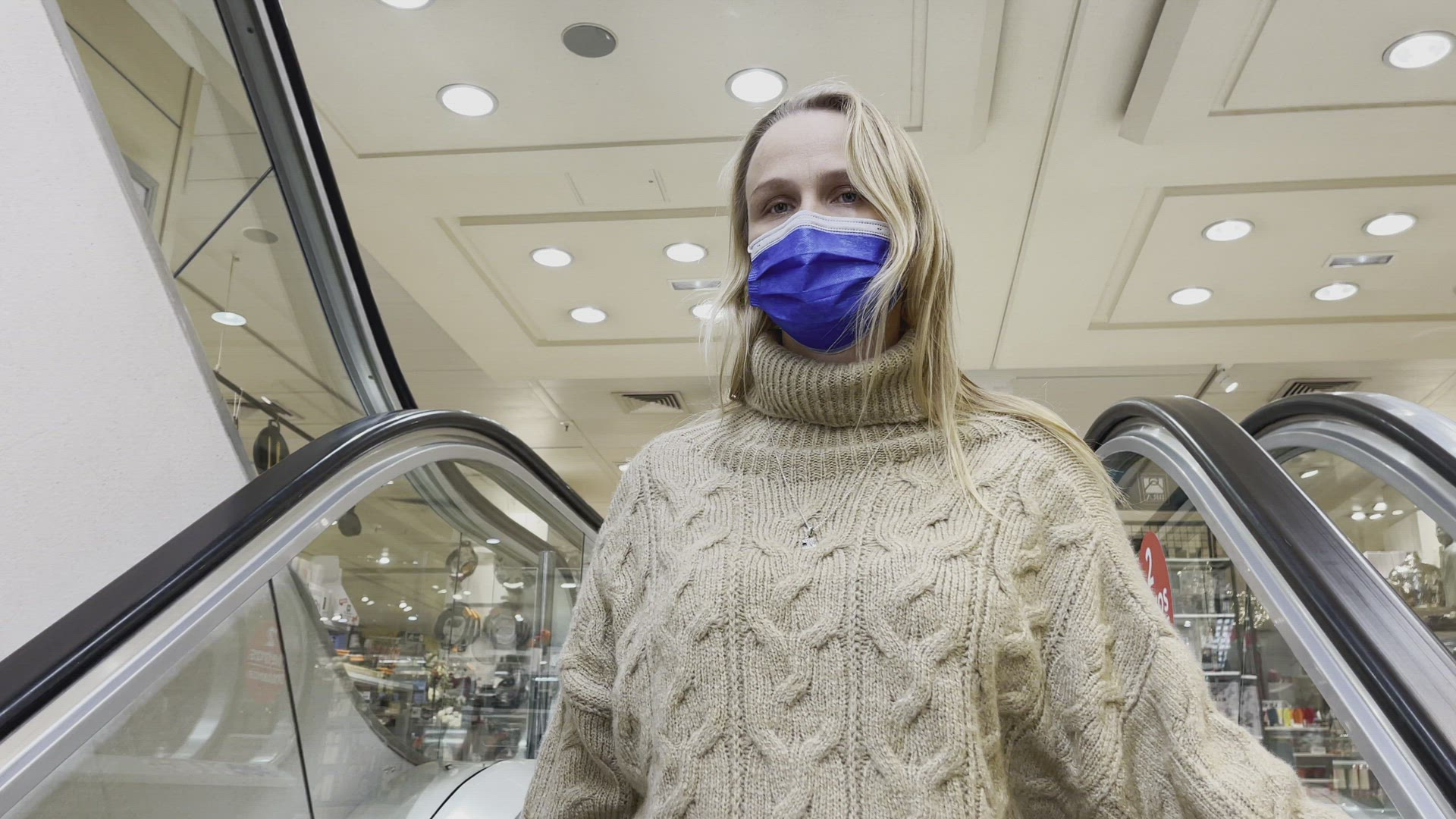 Woman customer in mask on escalator in shopping mall