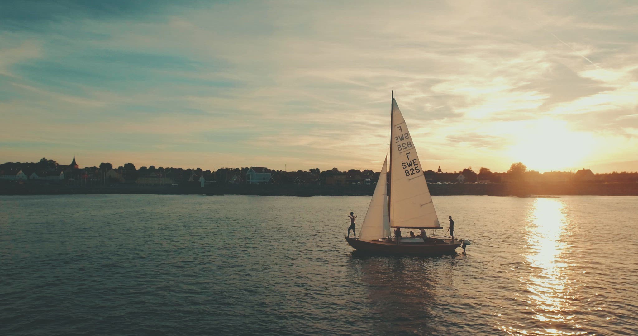 guy jumping of a sailboat aerial sunset coastline 4k