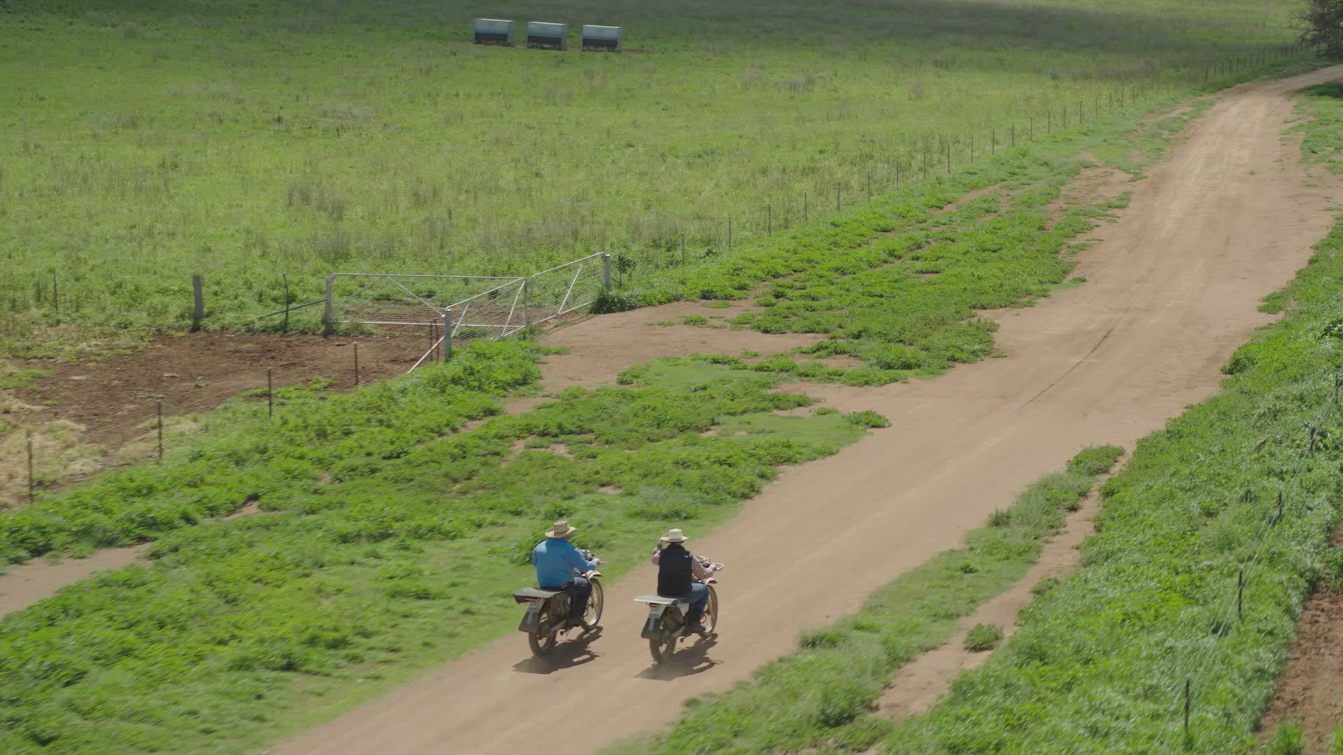 Two farmers ride motobikes through farm