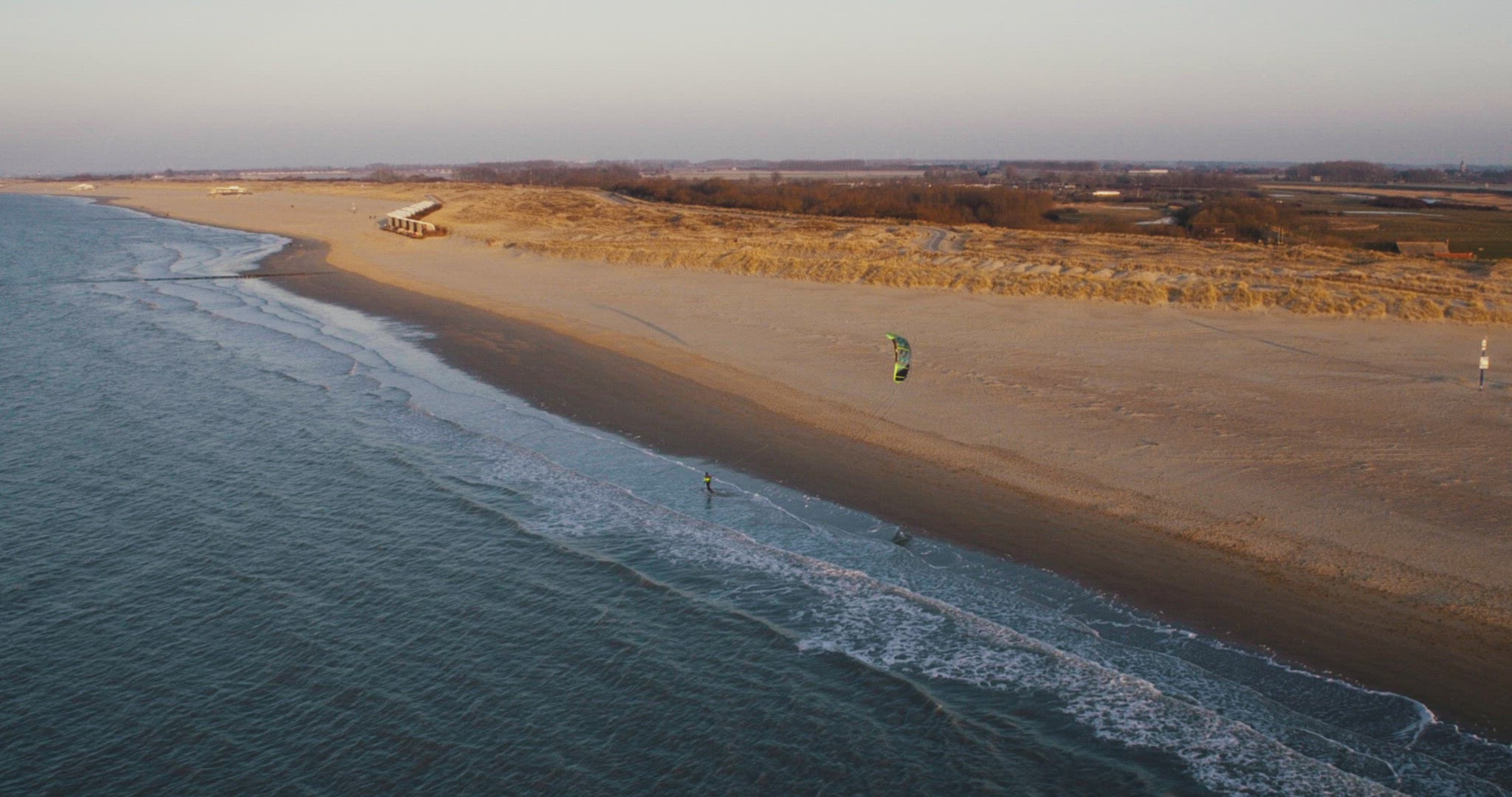 kitesurfer walking down the beach with kite sundown aerial
