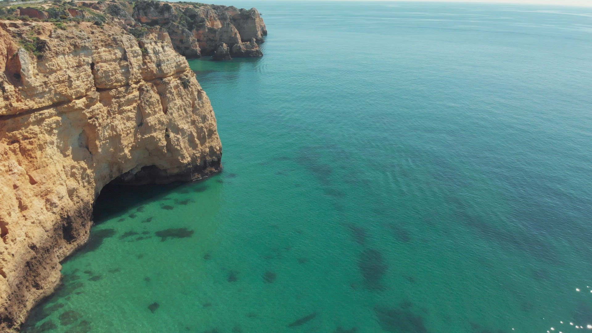 Vast turquoise ocean bared by Steep eroded cliffs in Lagos coast, Algarve, Portugal - Aerial fly-by 