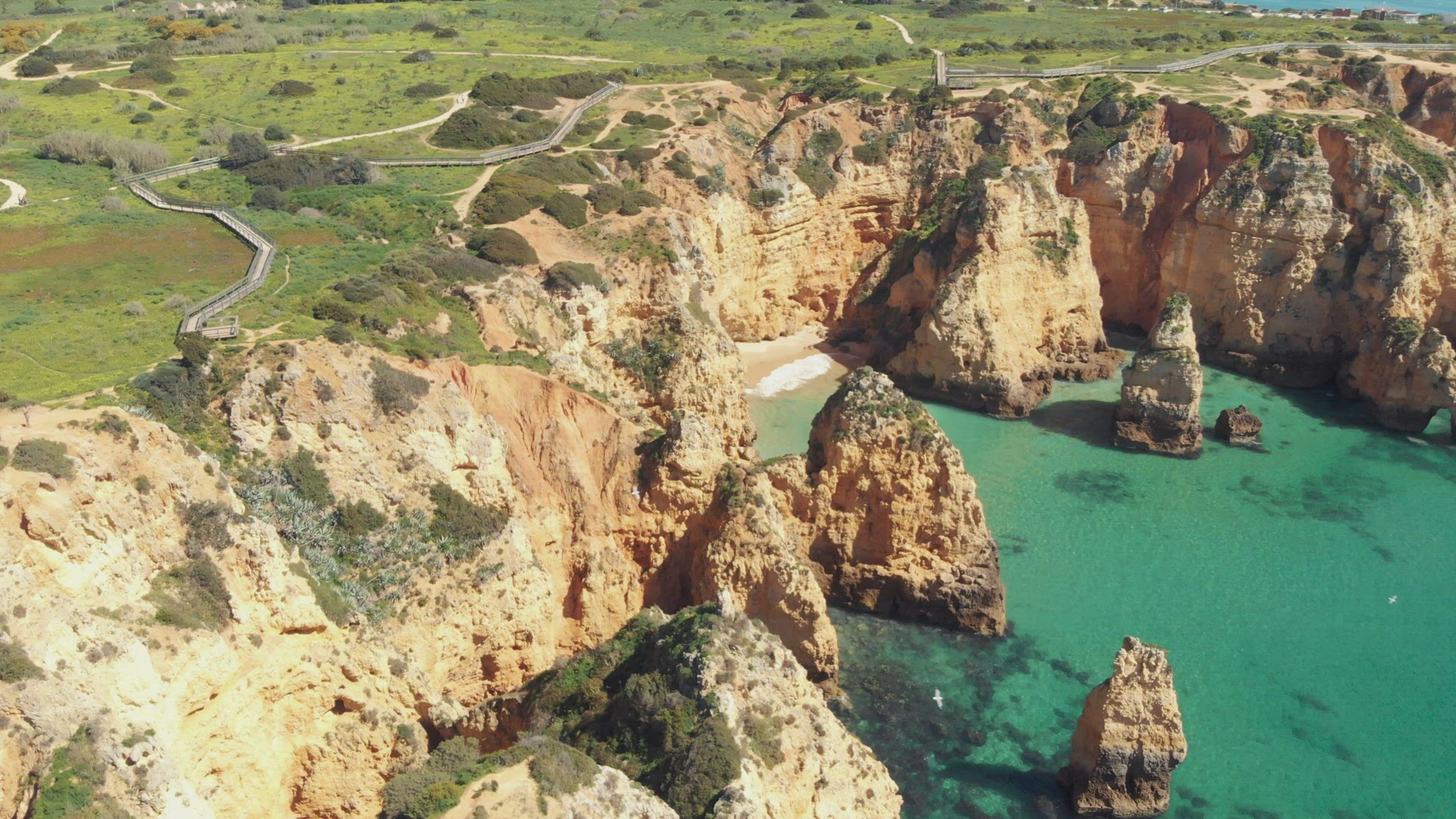 Emerald Green sea bathing Ponta da Piedade cliffs in Lagos Algarve, Portugal - Wide establishing sli