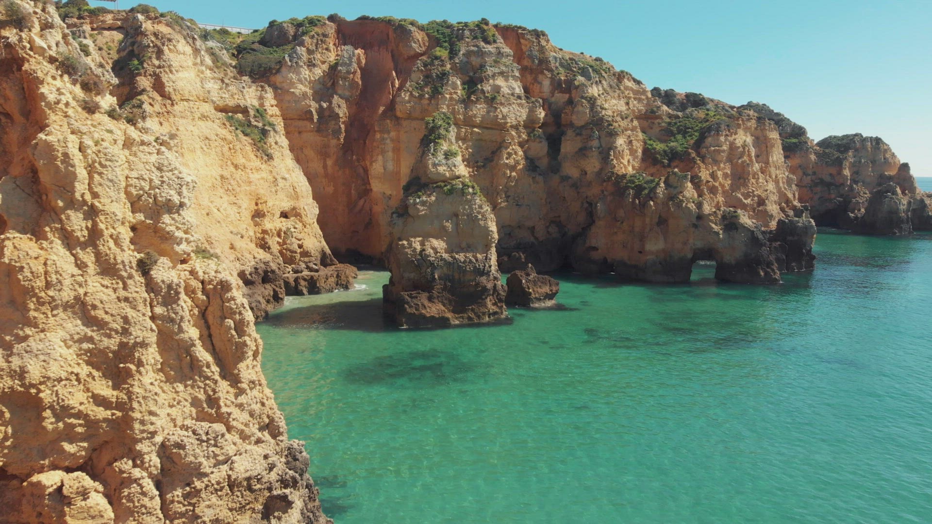 Craggy cliffs jutting out of crystal clear waters of the Algarve Sea, in Lagos, Portugal - Aerial gr