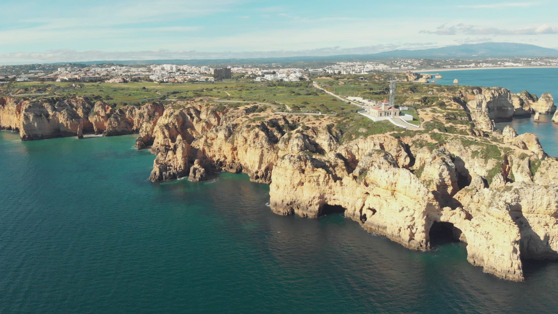 Ponta da Piedade lighthouse surrounded by barren headlands in Algarve - Wide Aerial top view slow Or