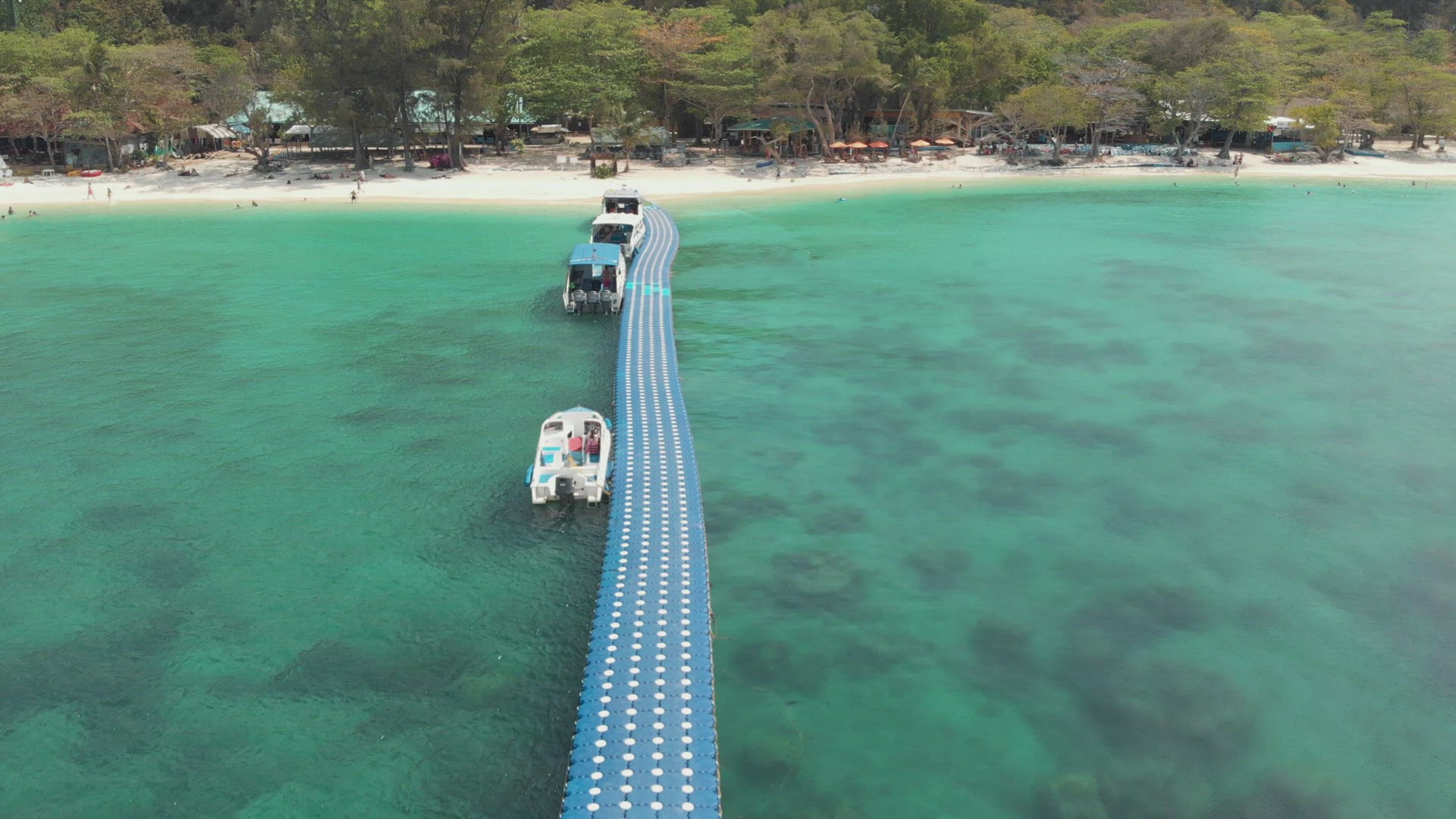 Approaching sand beach of Coral Island, Thailand. Fly over pier and boats