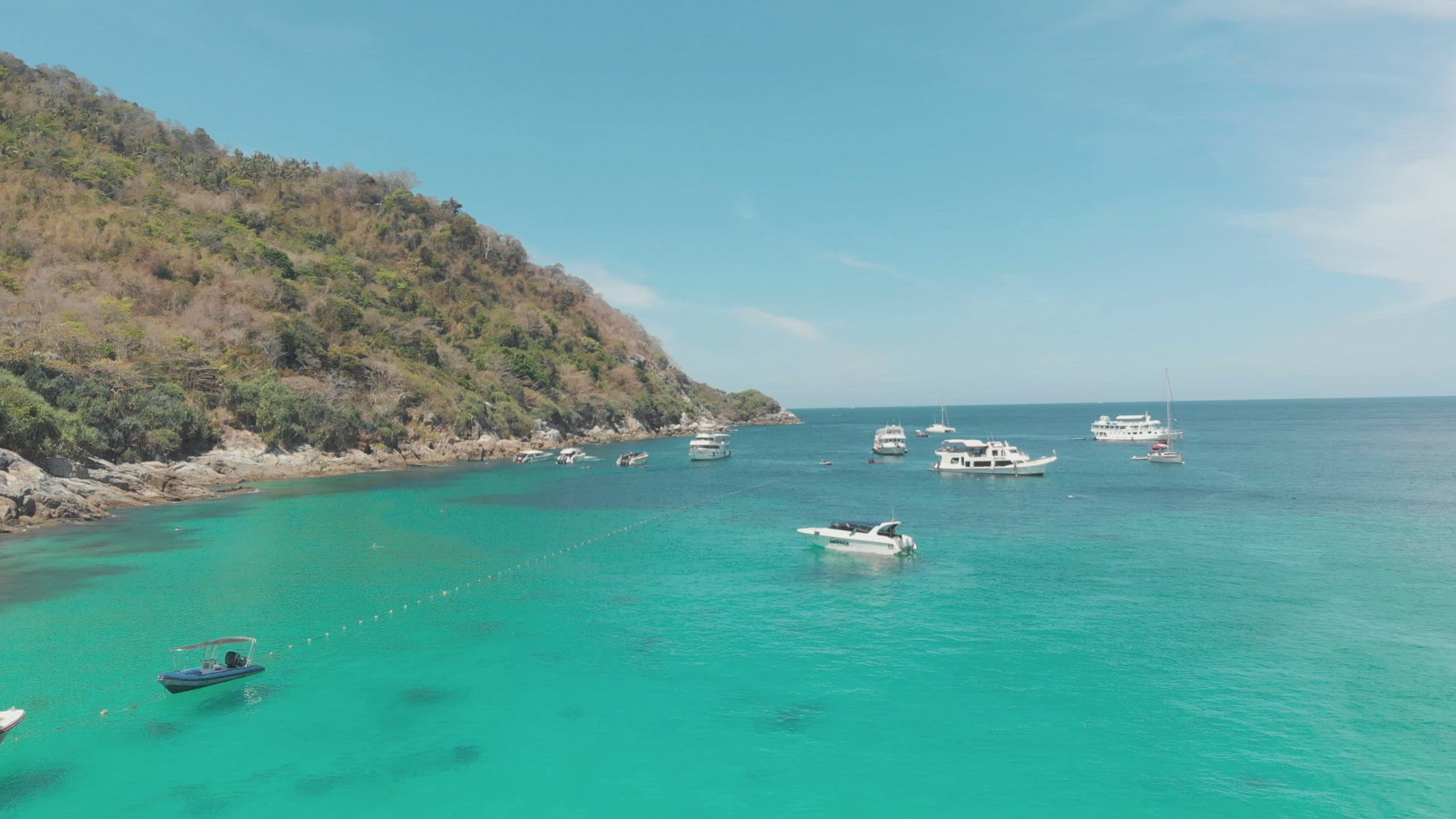 Yachts and Crystal clear blue waters surrounding the steep hill bordering the shore in Ko Racha Yai 