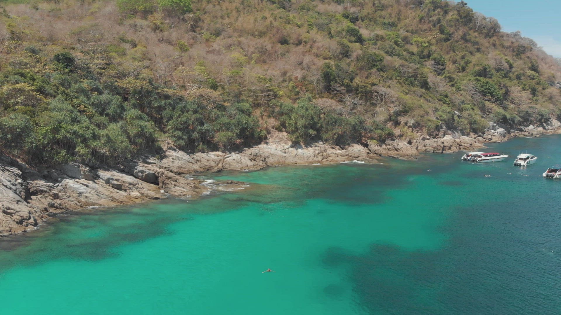 Emerald green waters protecting a coral reef and bordering a rocky shore and boat anchorage - Aerial