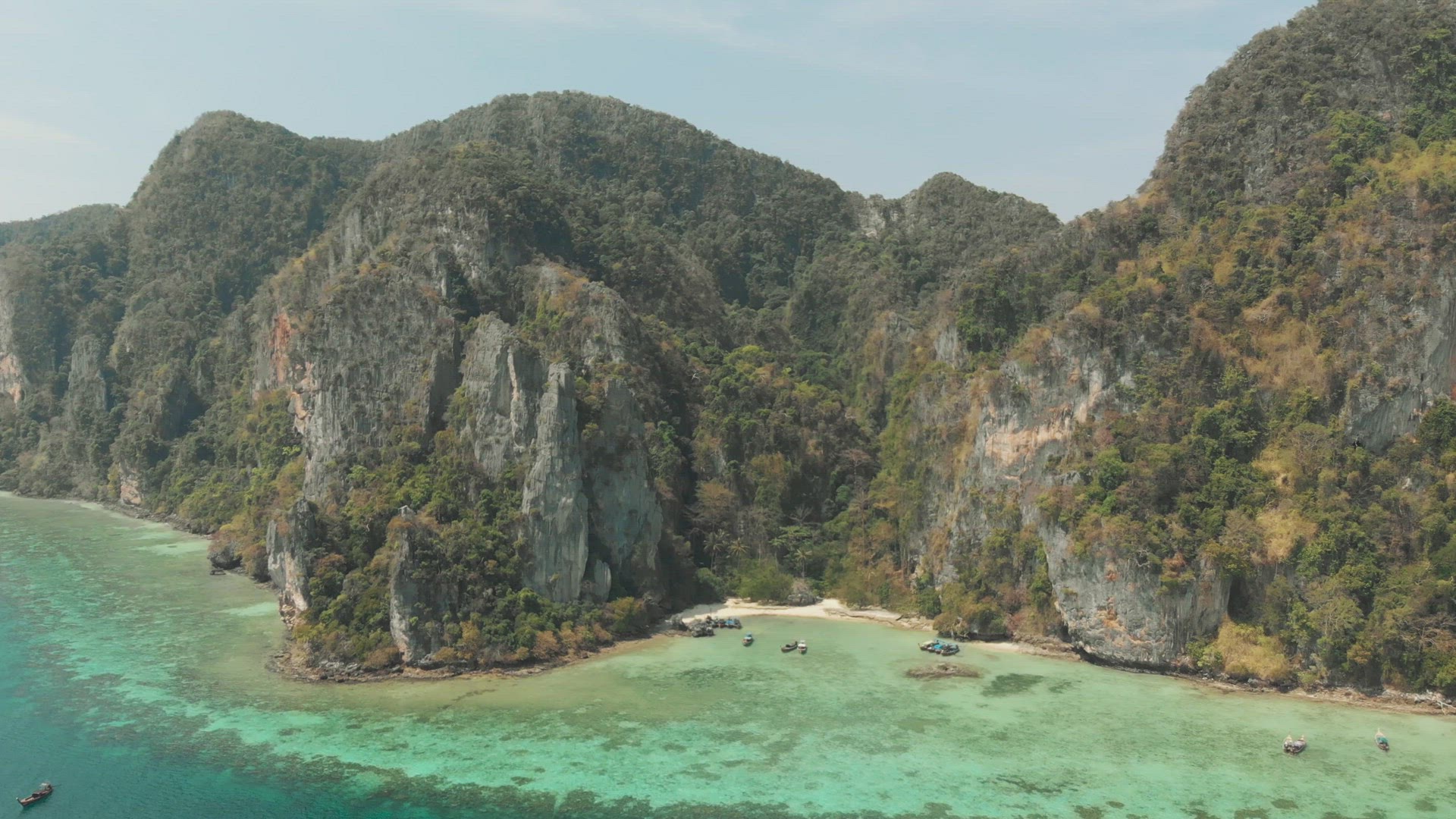 Tall Limestone cliffs  adjacent to shallow emerald green shoreline in Tonsai Bay, Ko Phi Phi Don Isl