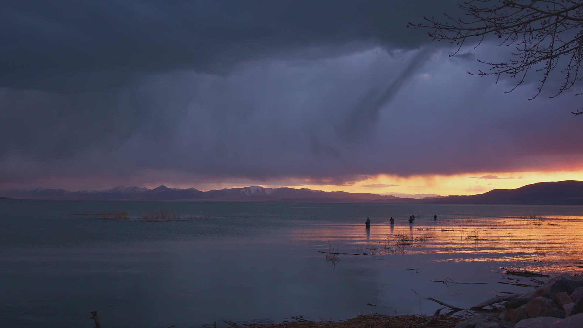 Streaks of rain fall over Utah Lake at dusk past fishermen