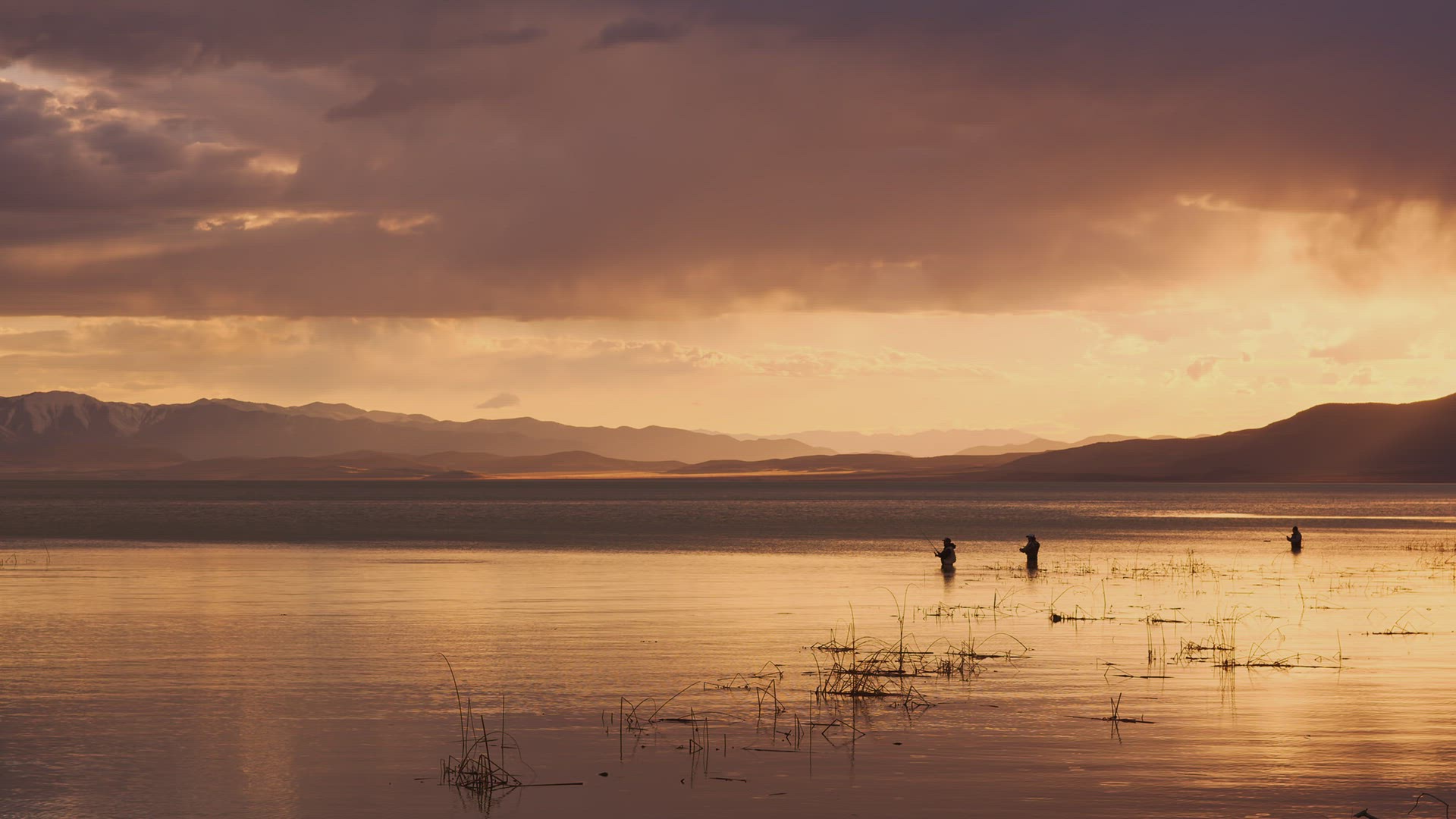 Rain falling in the distance past fishermen standing in Utah Lake