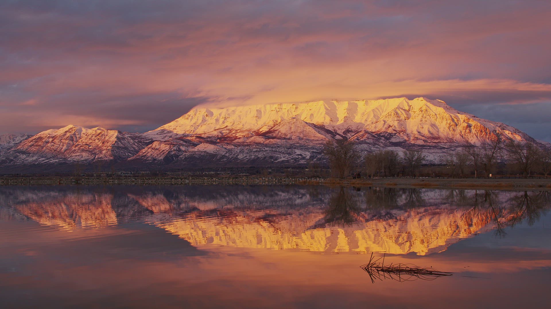 Snow capped mountain reflecting in water moving in slow motion at sunset