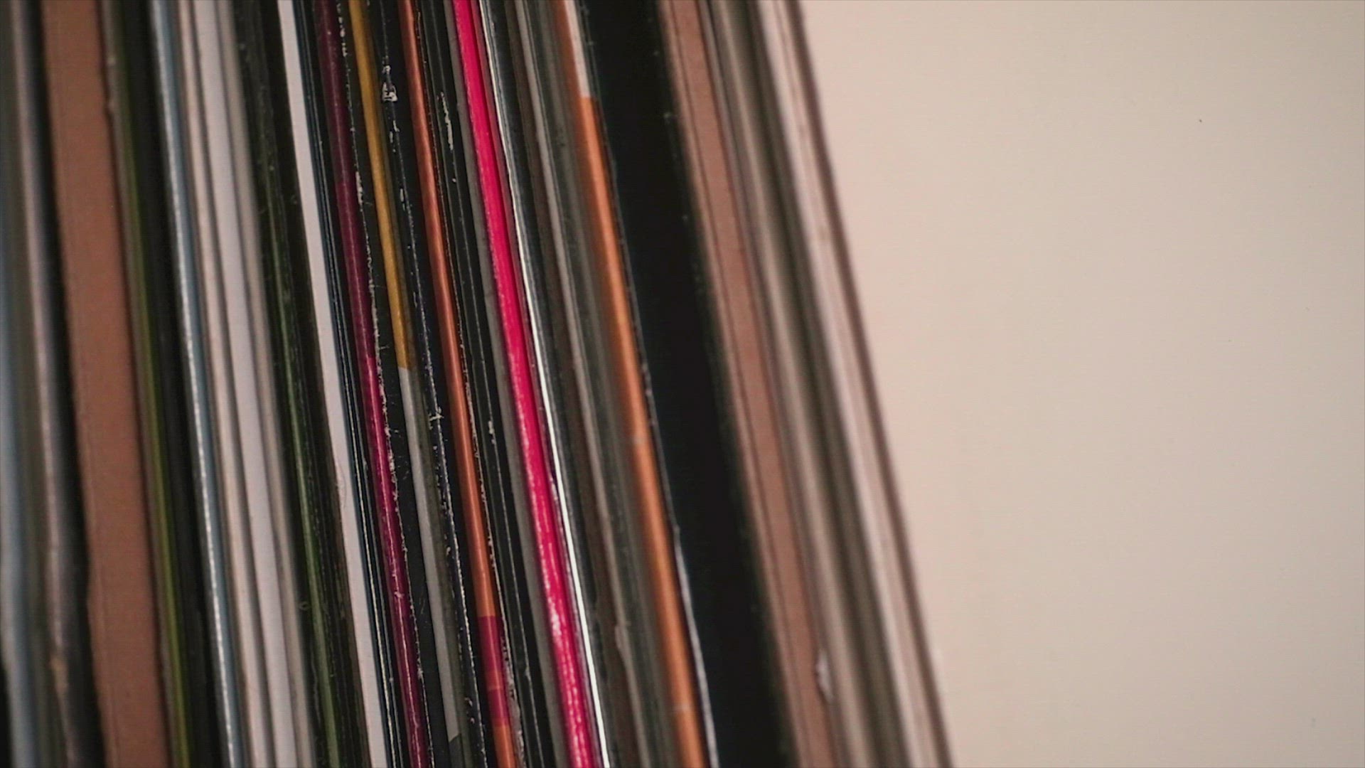 Slow dolly shot passing across a vinyl record collection, mans hand picks a white label  
