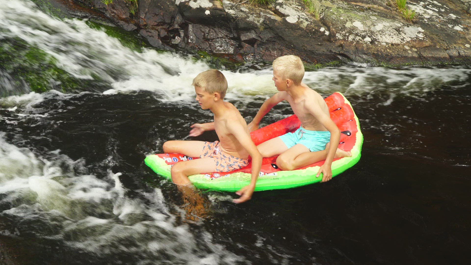 two boys playing with air mattress in streaming water