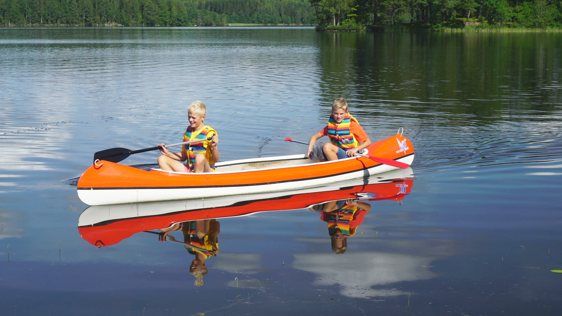 two boys paddling a canoe on lake in värmland - mirror lake