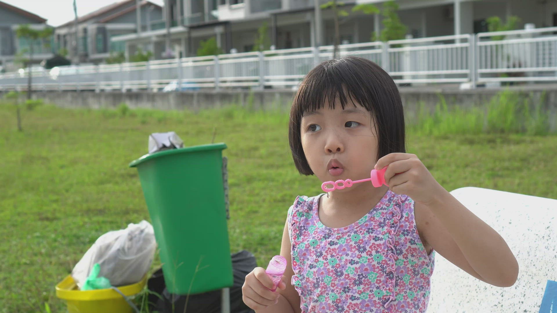 Little girl blow bubble beside rubbish bin
