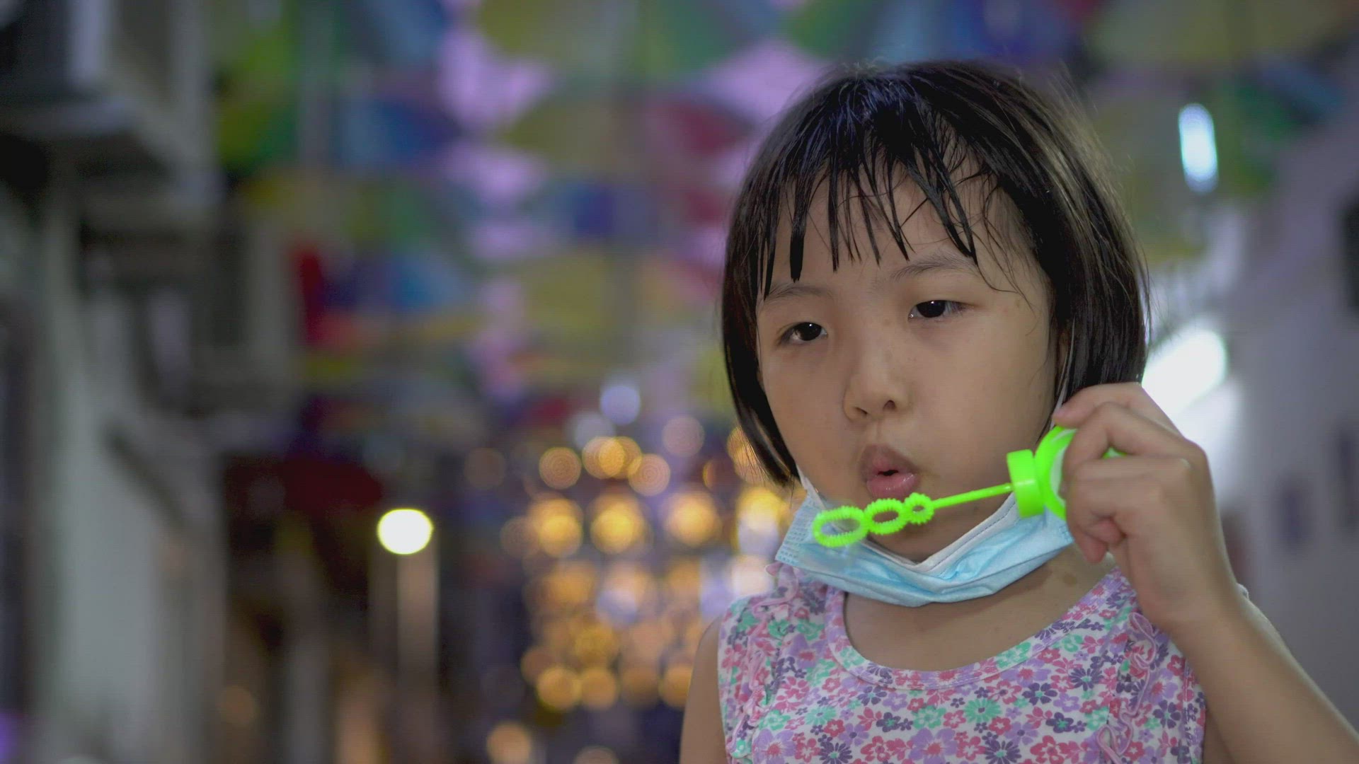 Asian girl with face mask at chin blow bubble at night