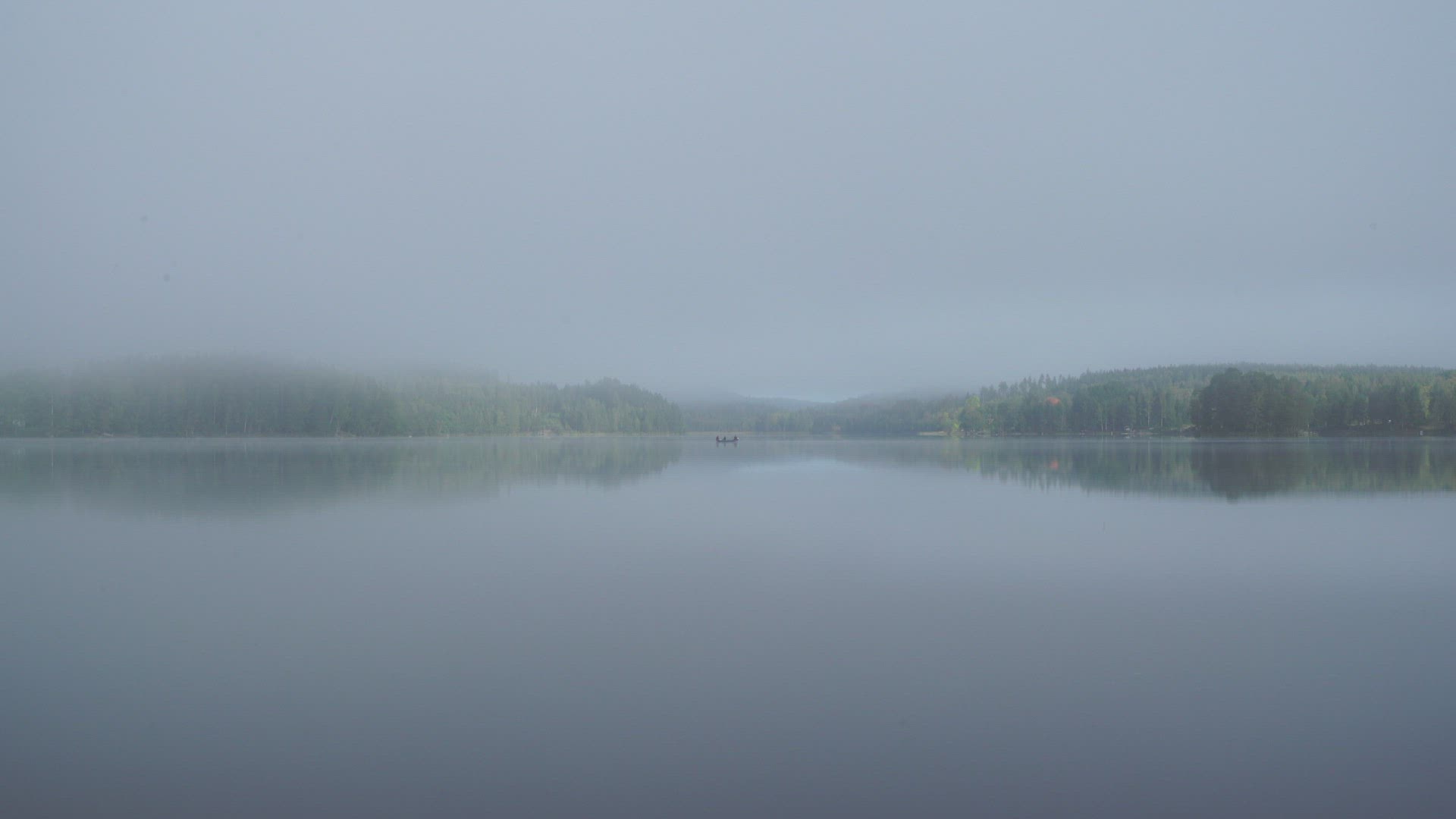 early morning - foggy misty lake - small boat in the distance