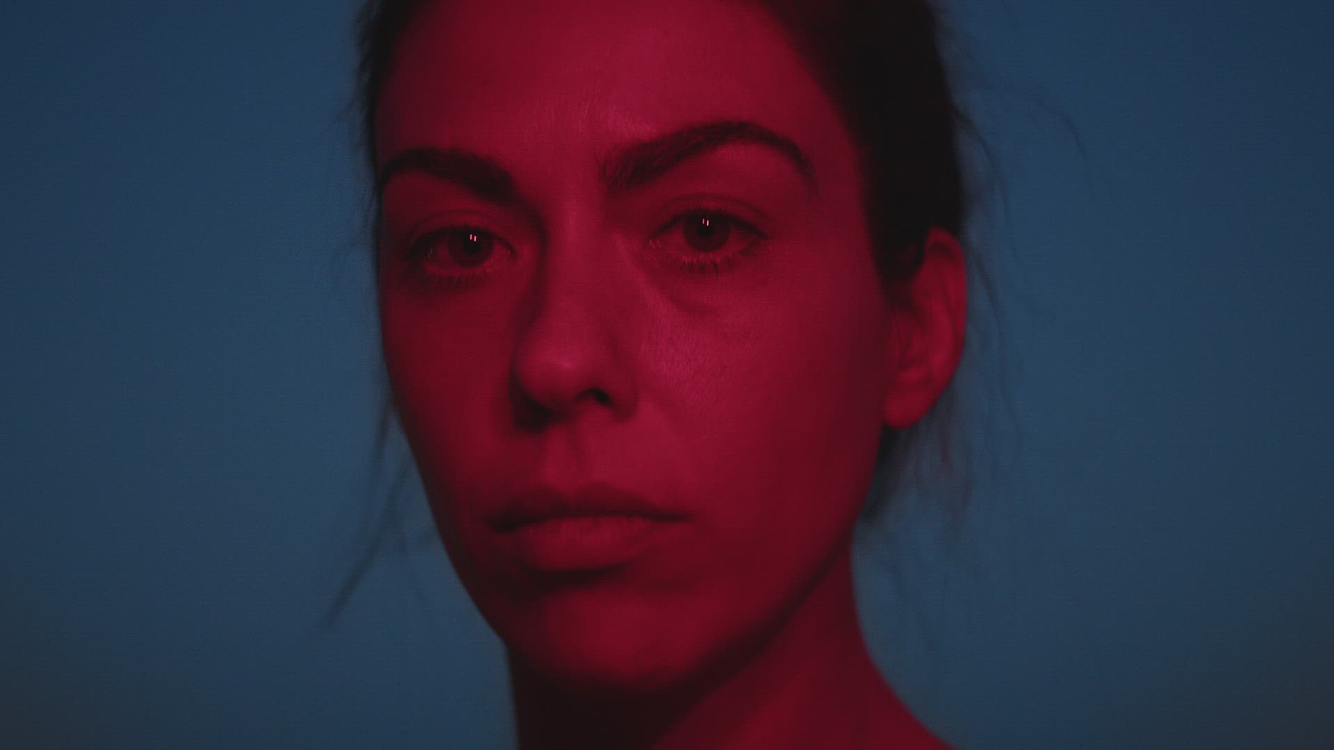 Woman looking at camera illuminated in red over blue sky