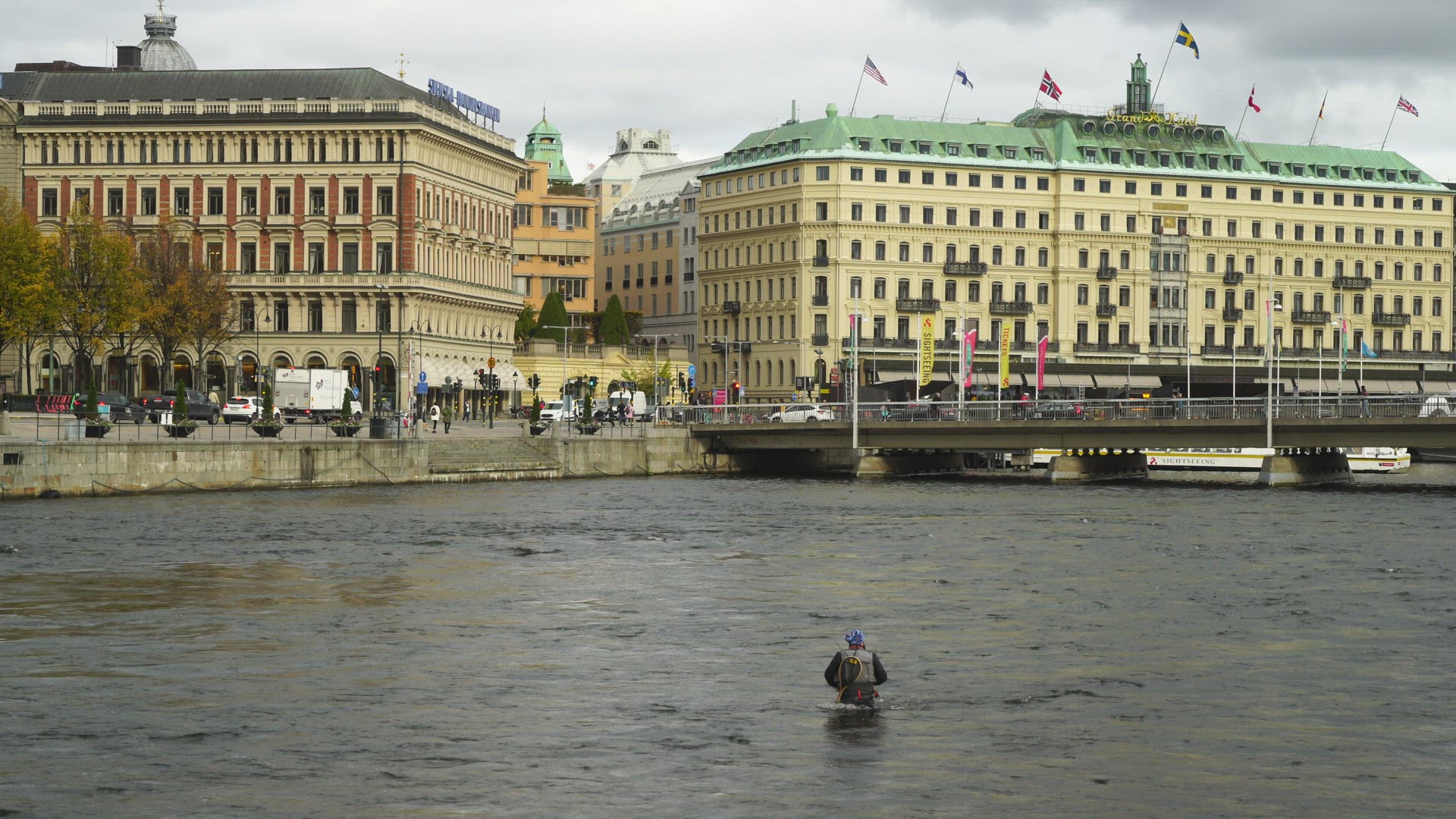 man fishing in central Stockholm - stands in streaming water close to Grand Hotel