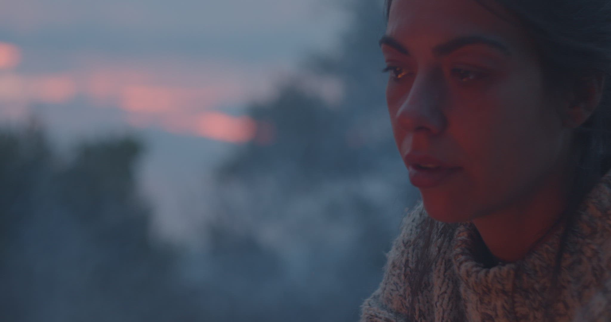 Seated woman looks bonfire at sunset