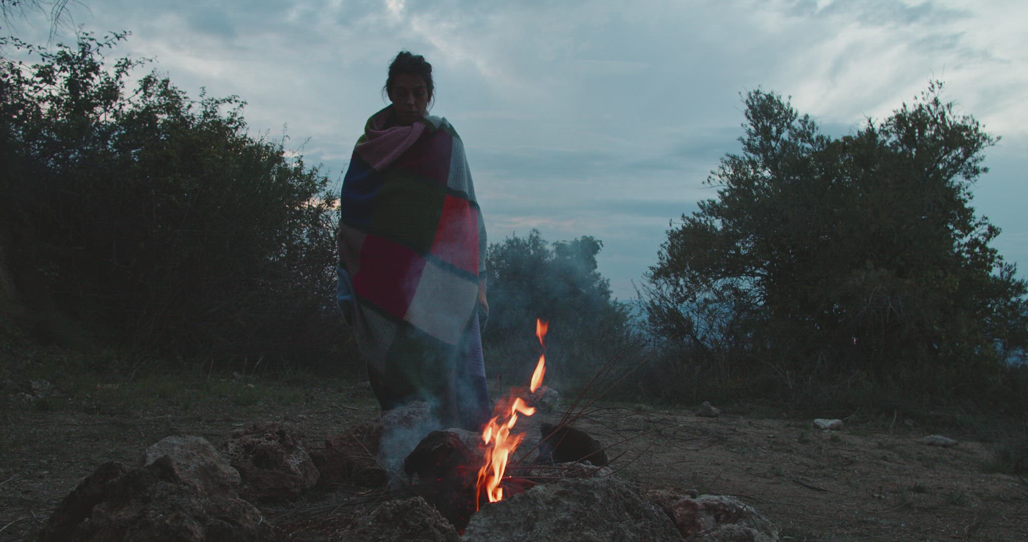 Woman covered with a blanket looks at a bonfire