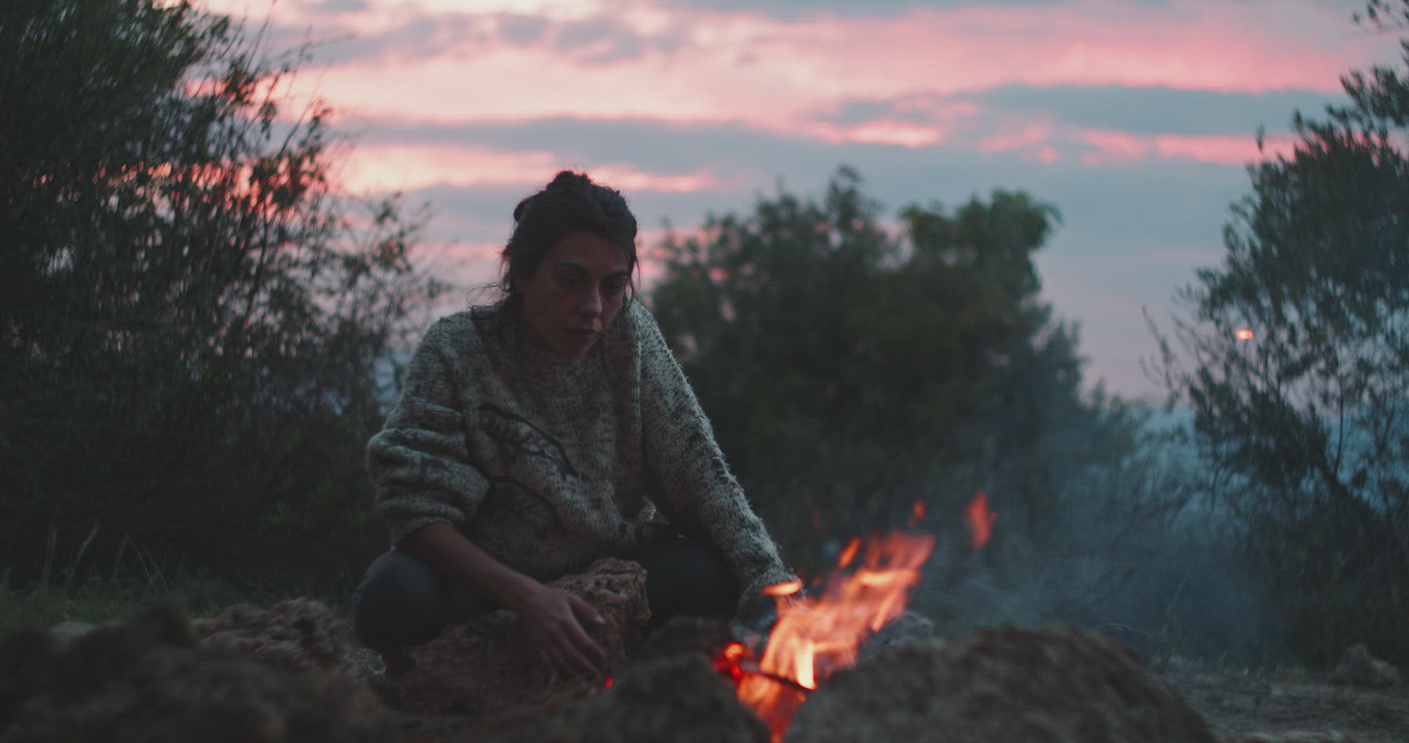 Woman crouching in front of a bonfire