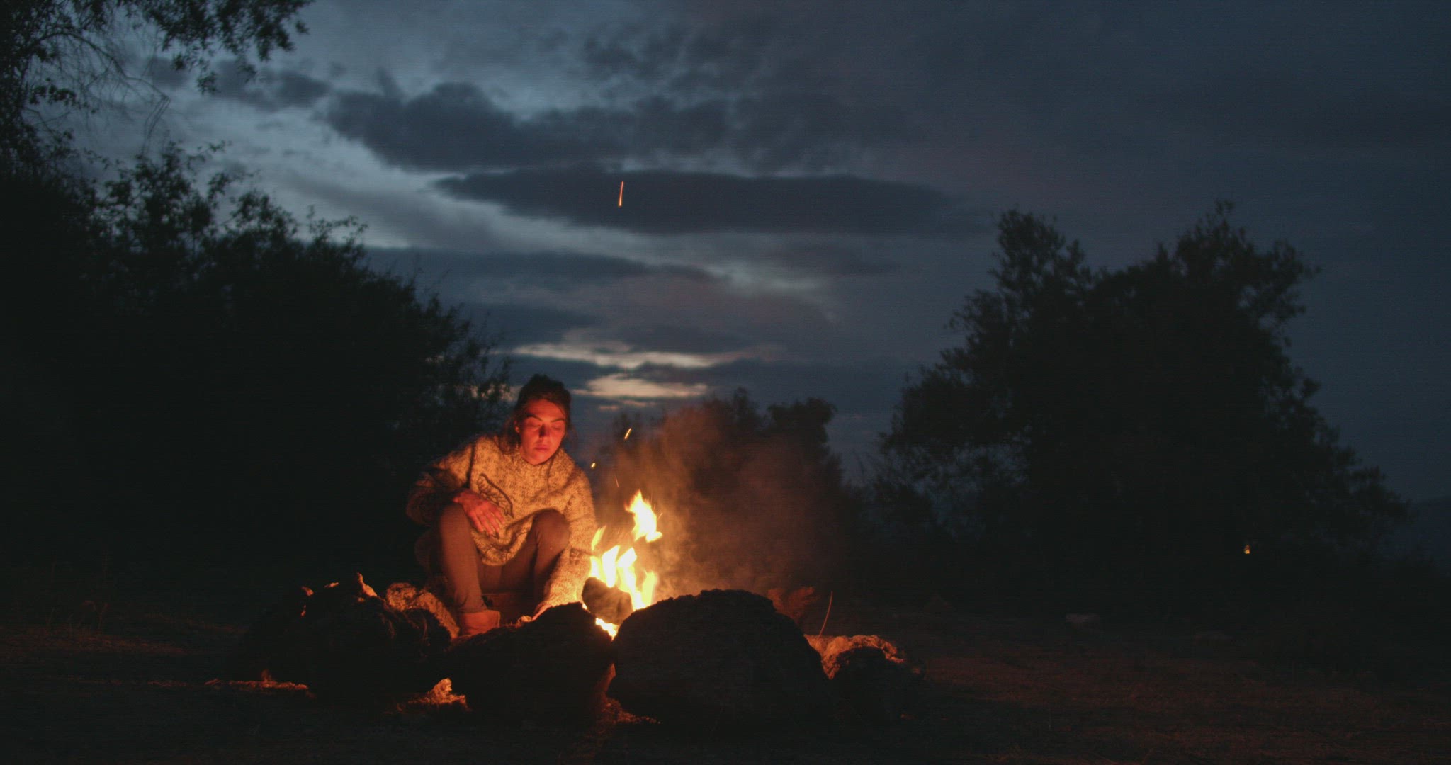 Woman sitting in the heat of the fire at dusk