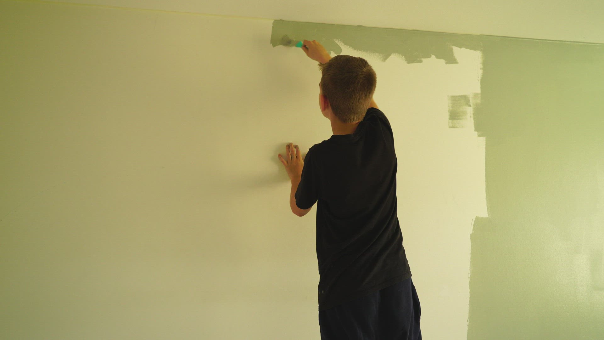 boy painting wall in green colour - paints with brush