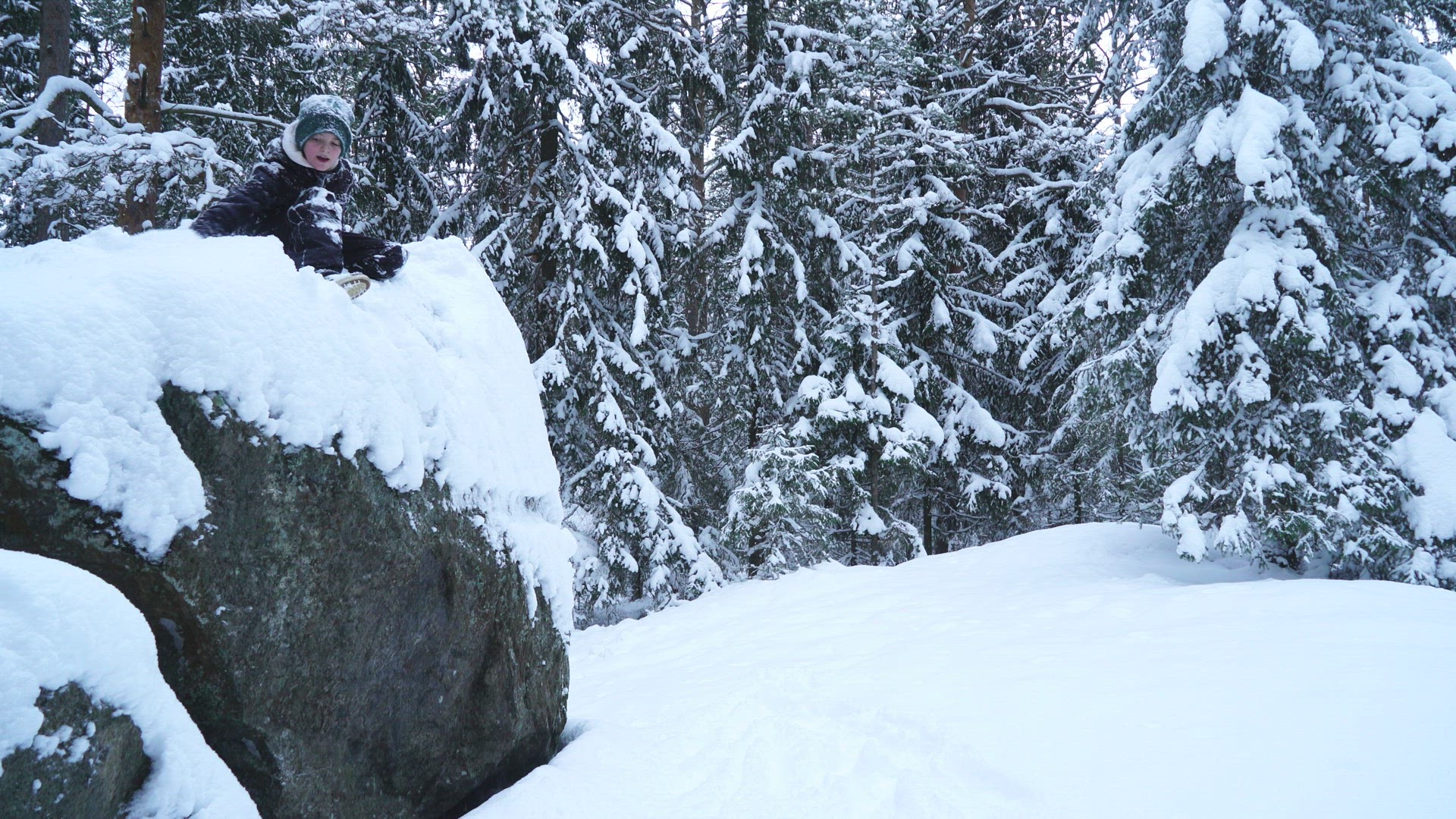 boy jumping from big stone into deep snow in forest