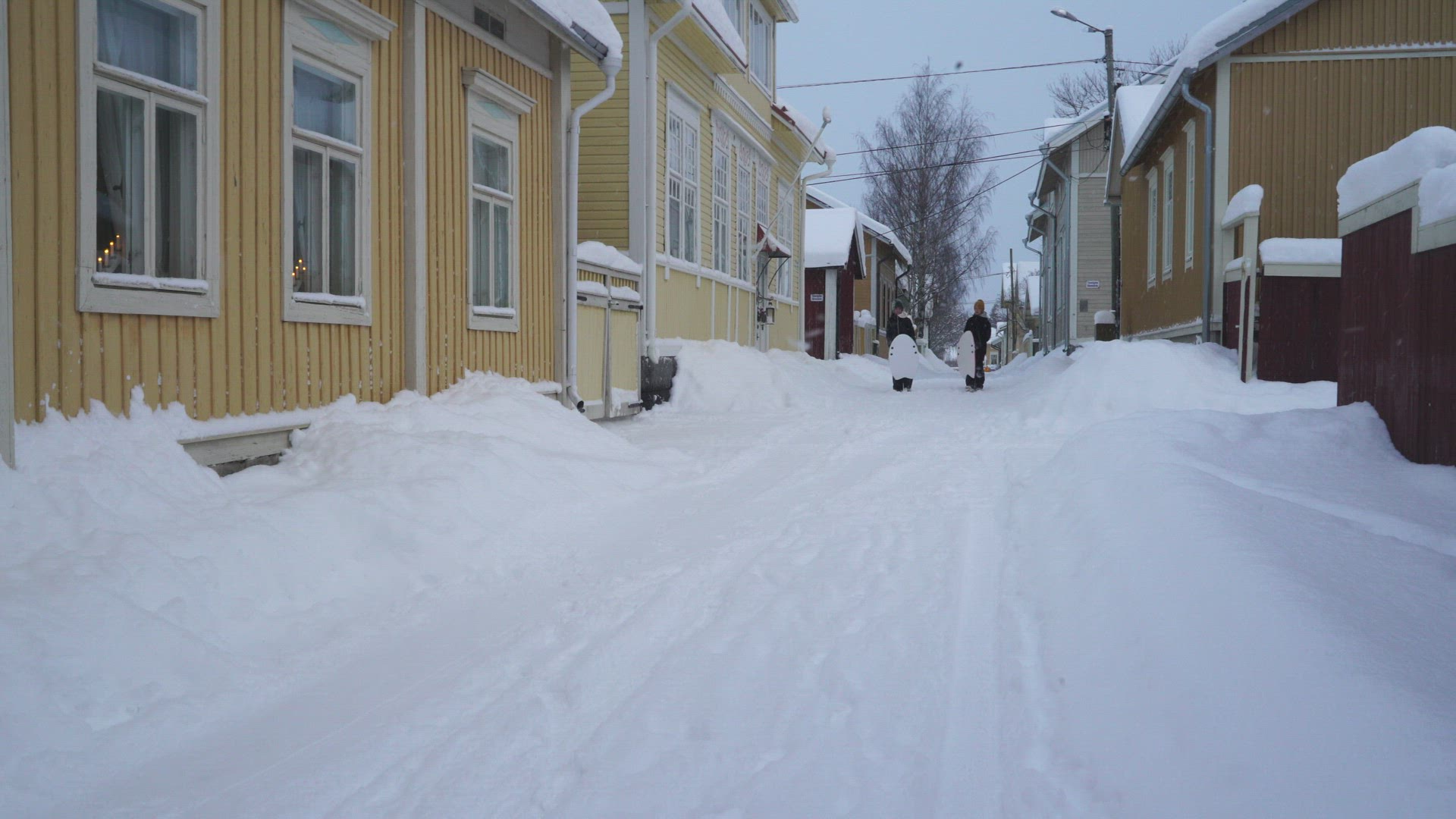 boys with toboggans sliding on snow in small city street 