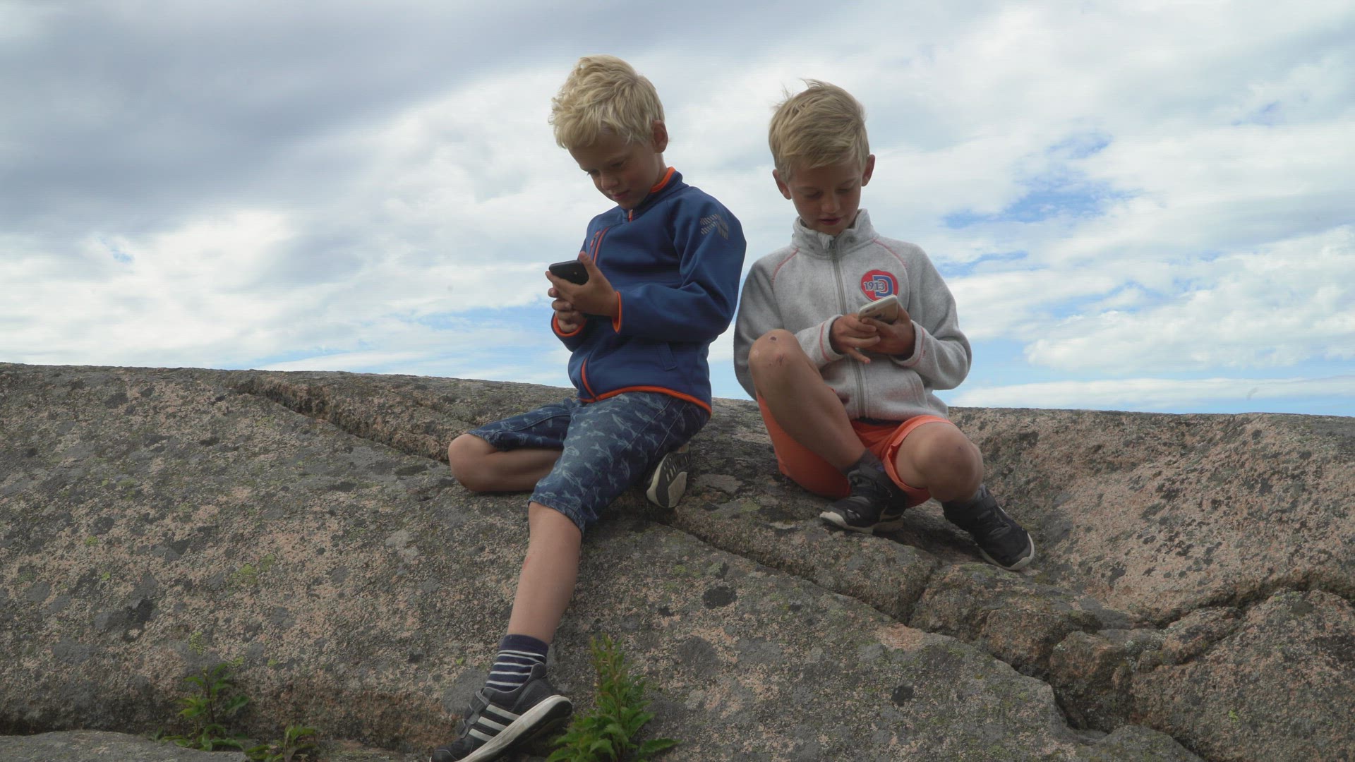 boys sitting on cliff - playing pokemon go