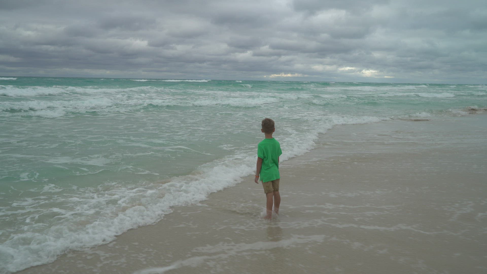 boy standing on beach - looking at waves and dramatic clouds