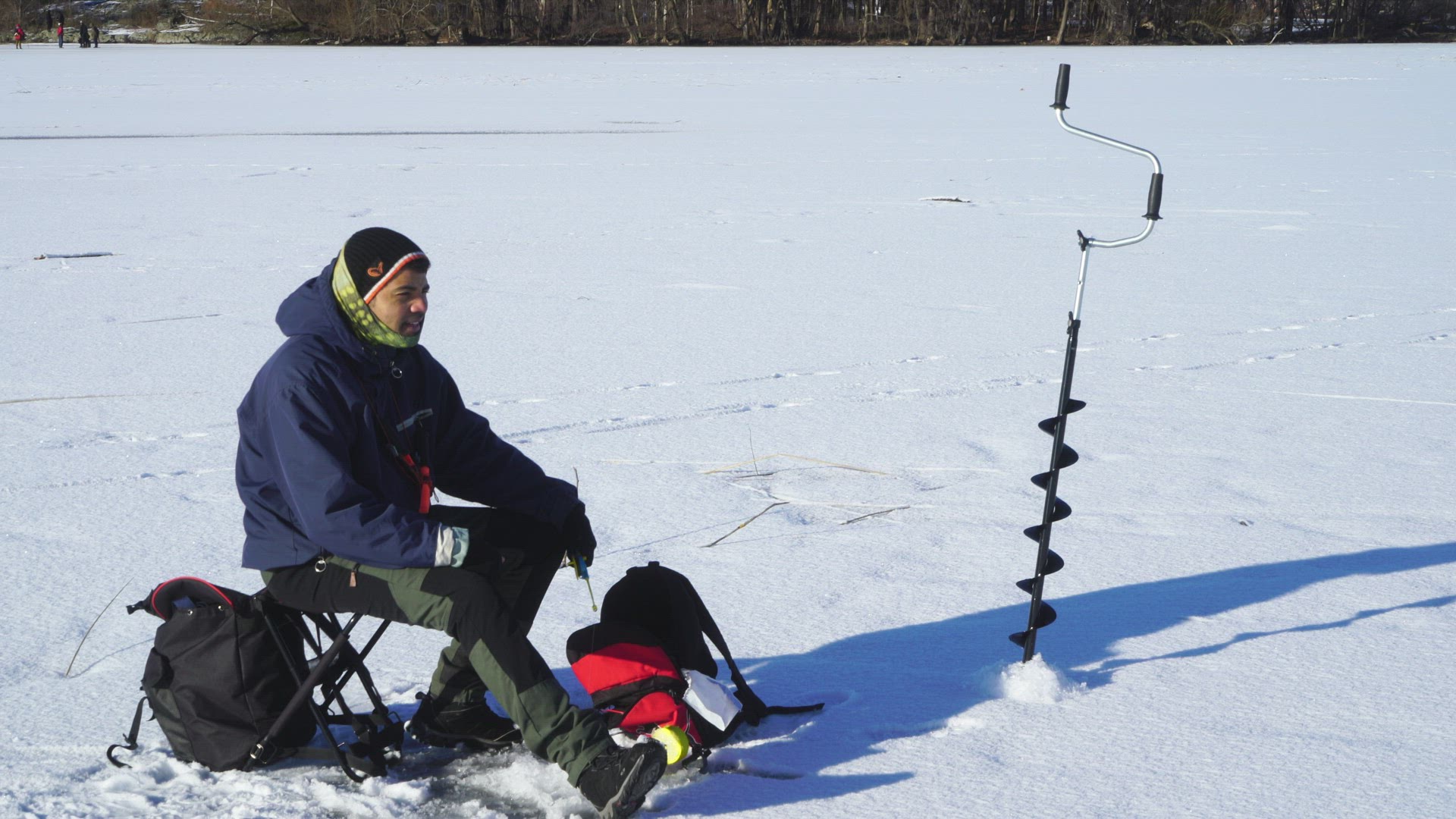 man sitting on lakes ice fishing - sunny winter day