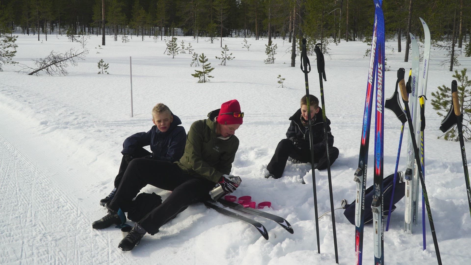mother and two children sitting on skis in snow - hot chocolate in thermos