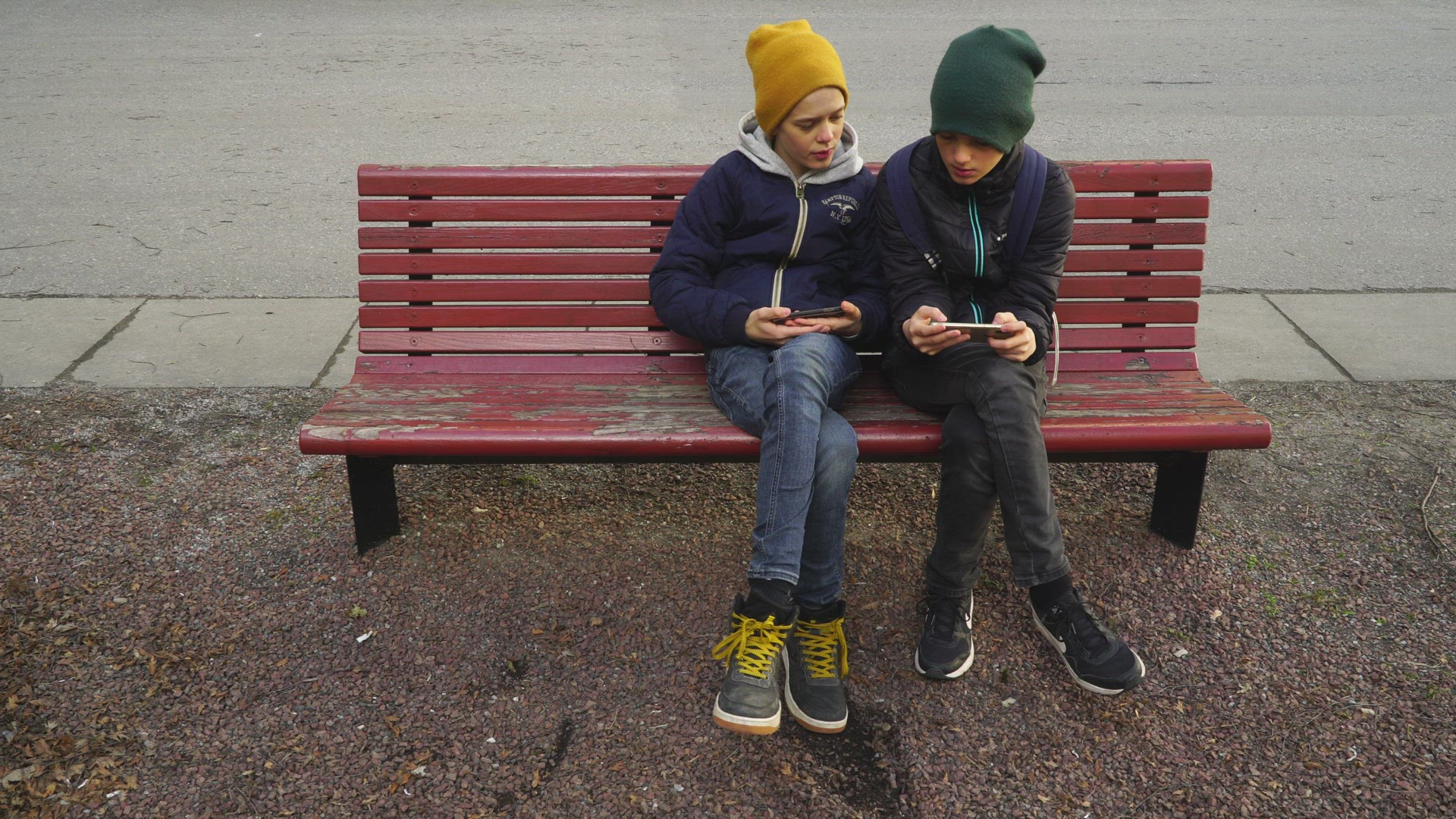 two boys sitting on bench - playing with mobile phones
