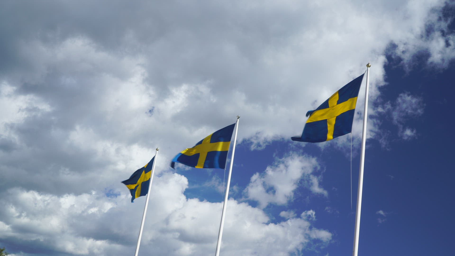 three swedish flags on flagpoles in strong wind - blue sky with white clouds