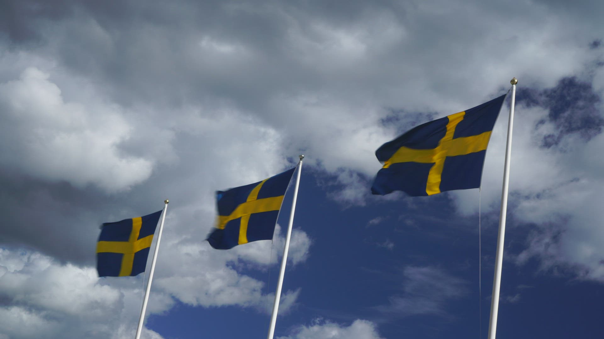 three swedish flags in strong wind - blue sky with white clouds