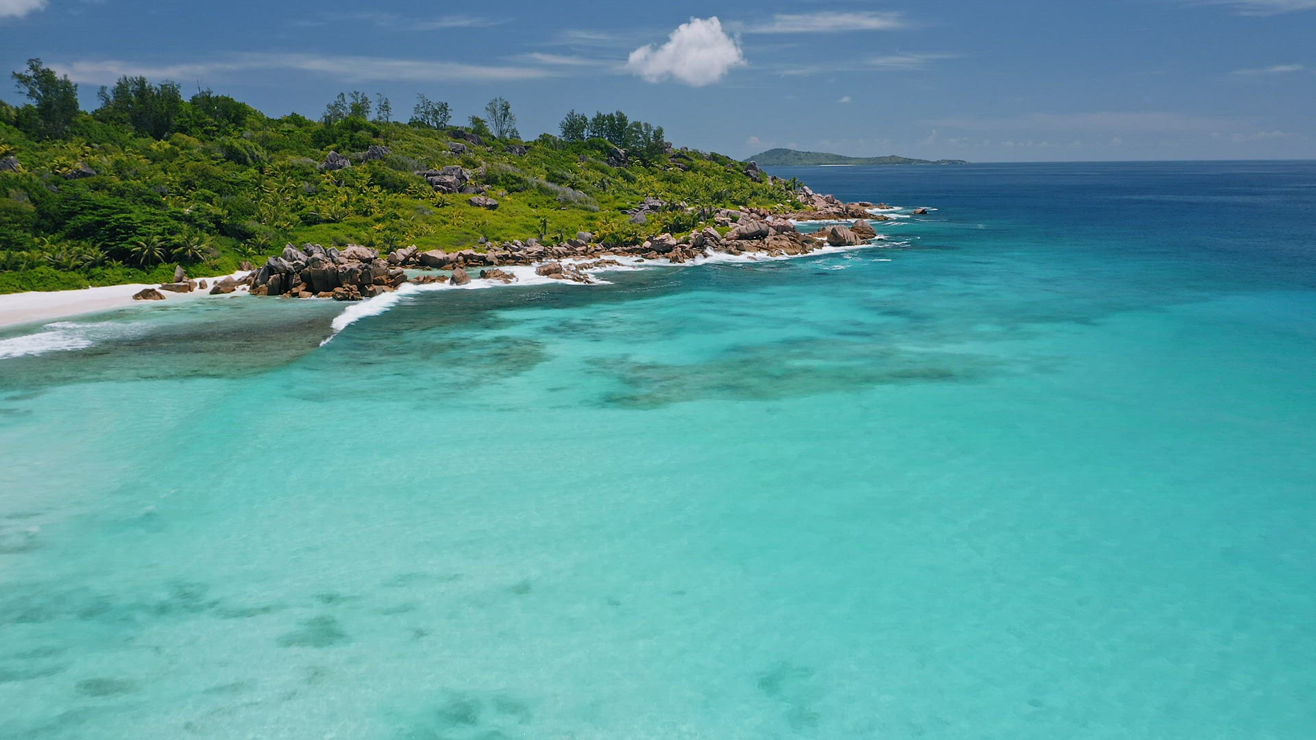 Aerial view over blue lagoon of Anse Coco tropical paradise beach. Ocean crystal clear waves rolling