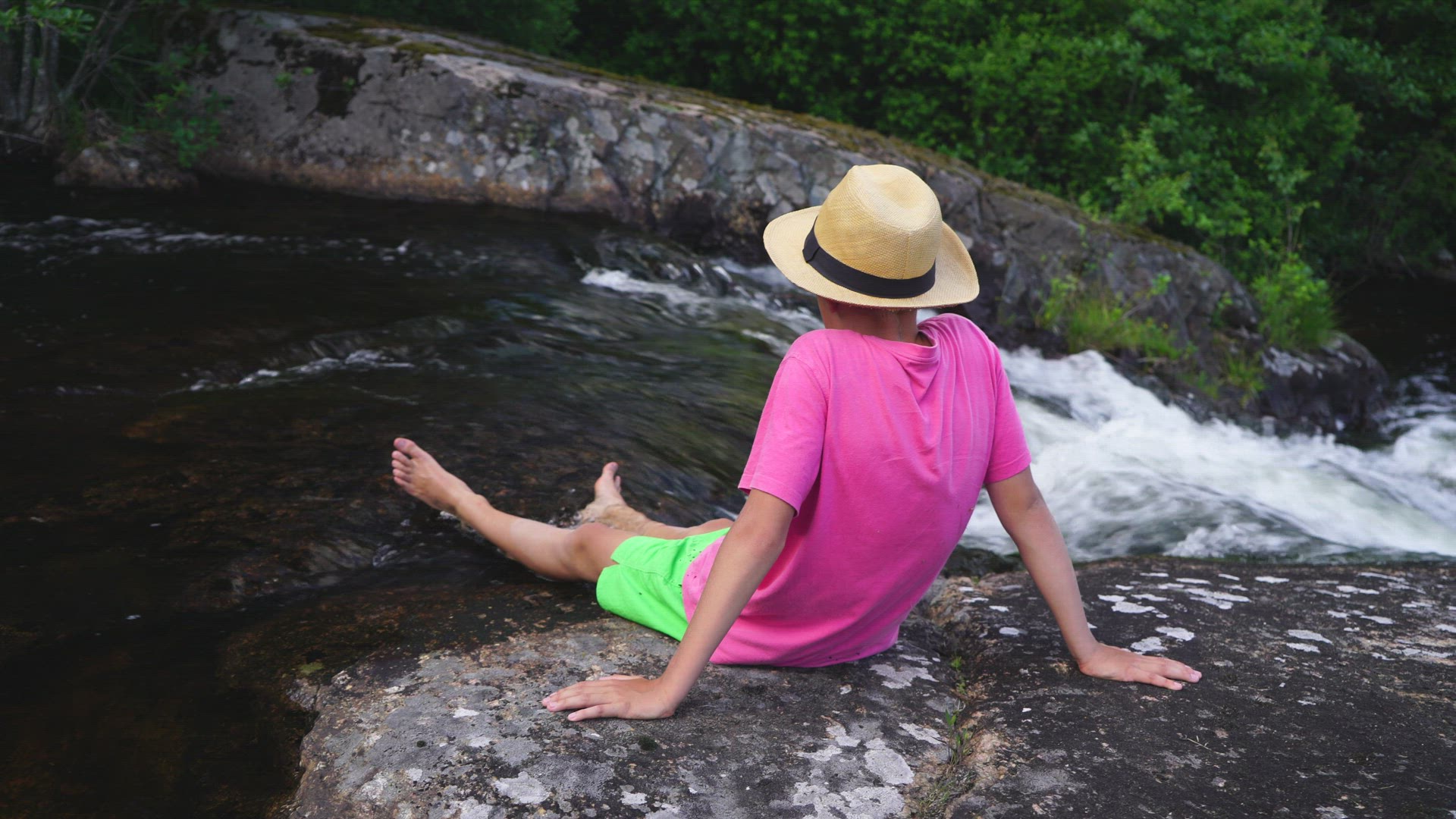 boy sitting close to waterfall with feet in streaming water