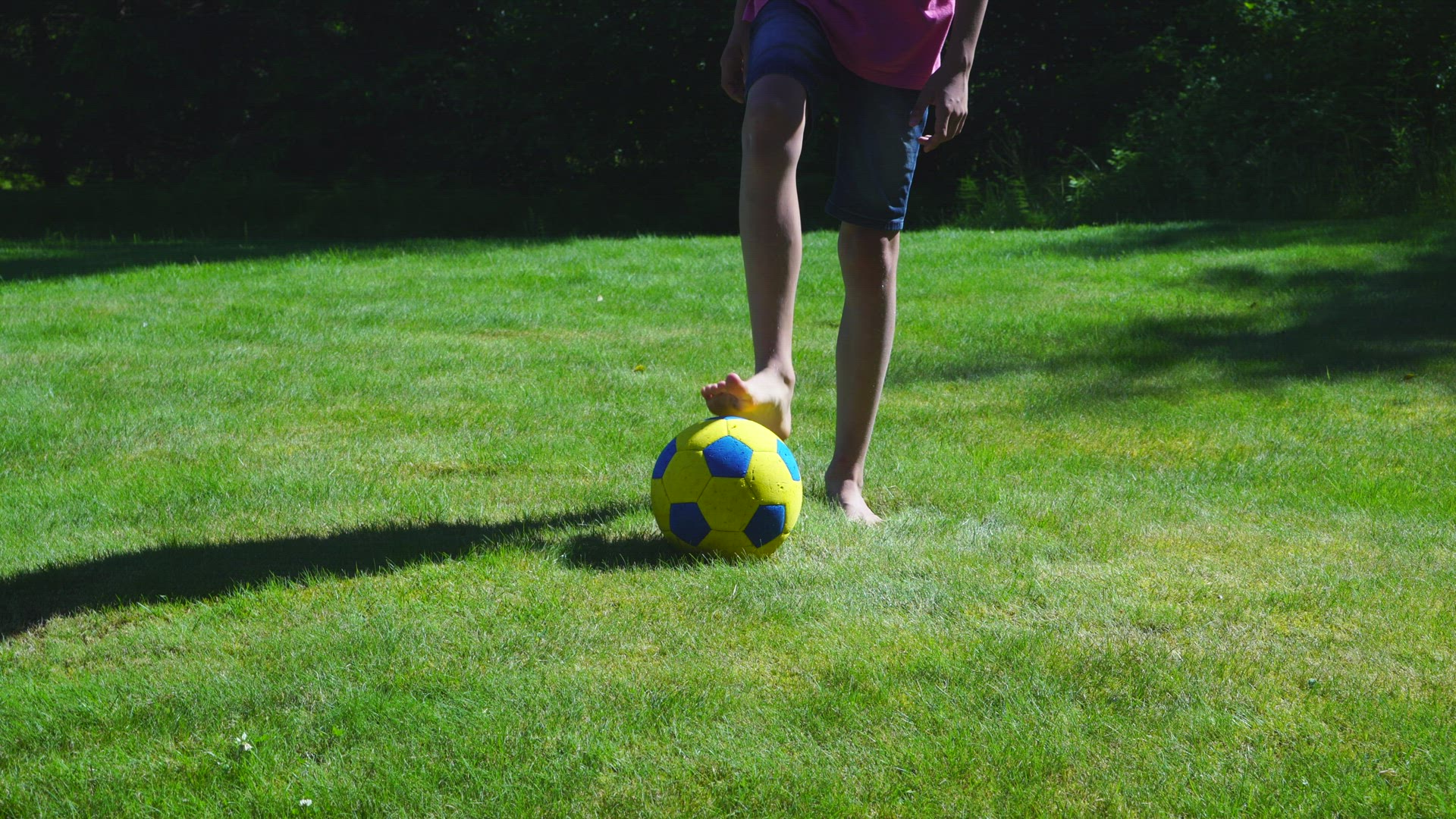 boy kicking with soccer ball in grass - barefoot