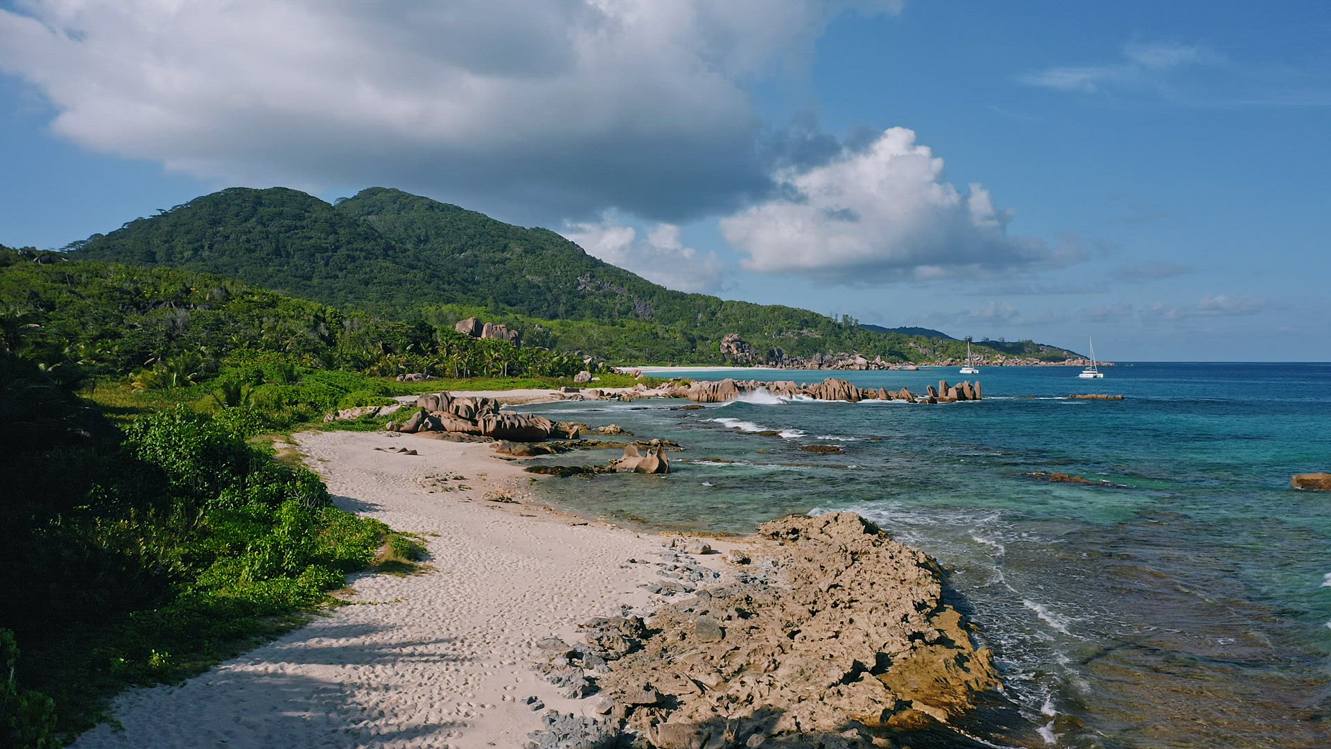 Aerial drone footage of tropical coastline with granite rocks and ocean waves rolling against shore.