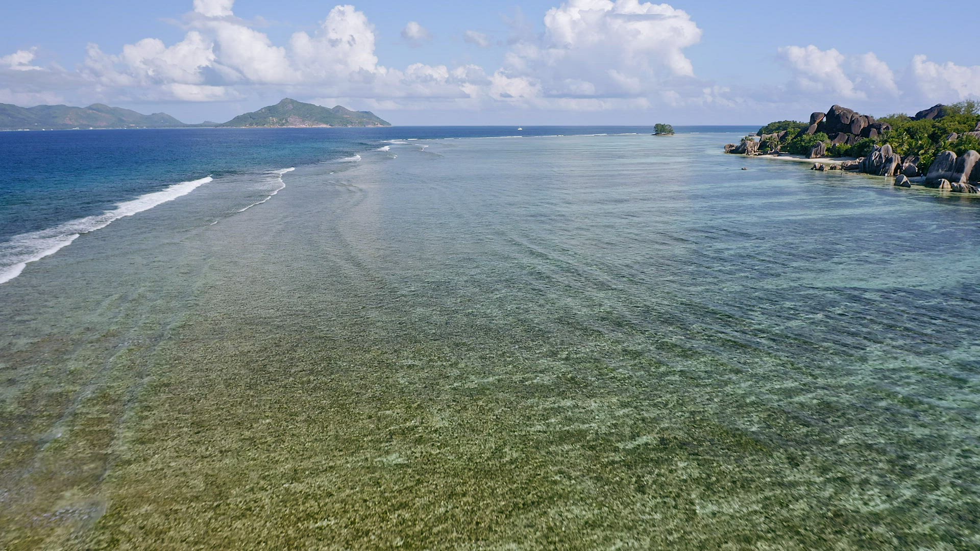 Aerial drone fly footage along tropical coast in sunny day time. Ocean waves rolling to famous Anse 