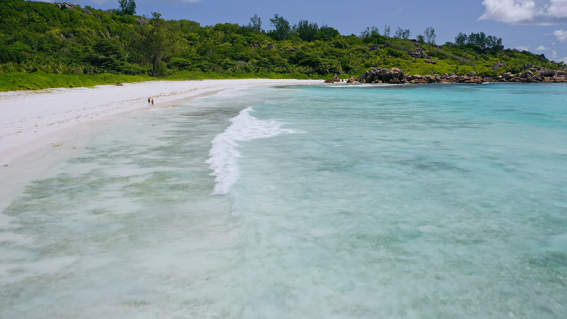 Aerial low altitude fly footage over tropical white sand beache with white rolling waves in turquois