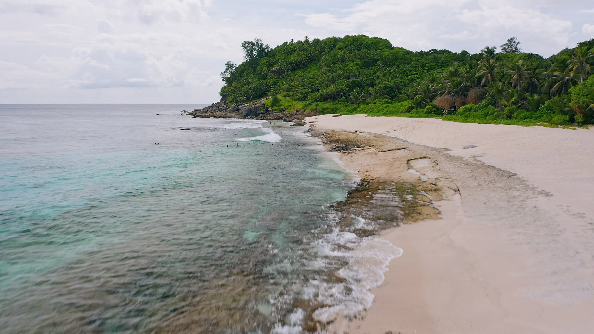Mahe island, Seychelles. Aerial low altitude fly on exotic sandy beach with tourists playing in wave