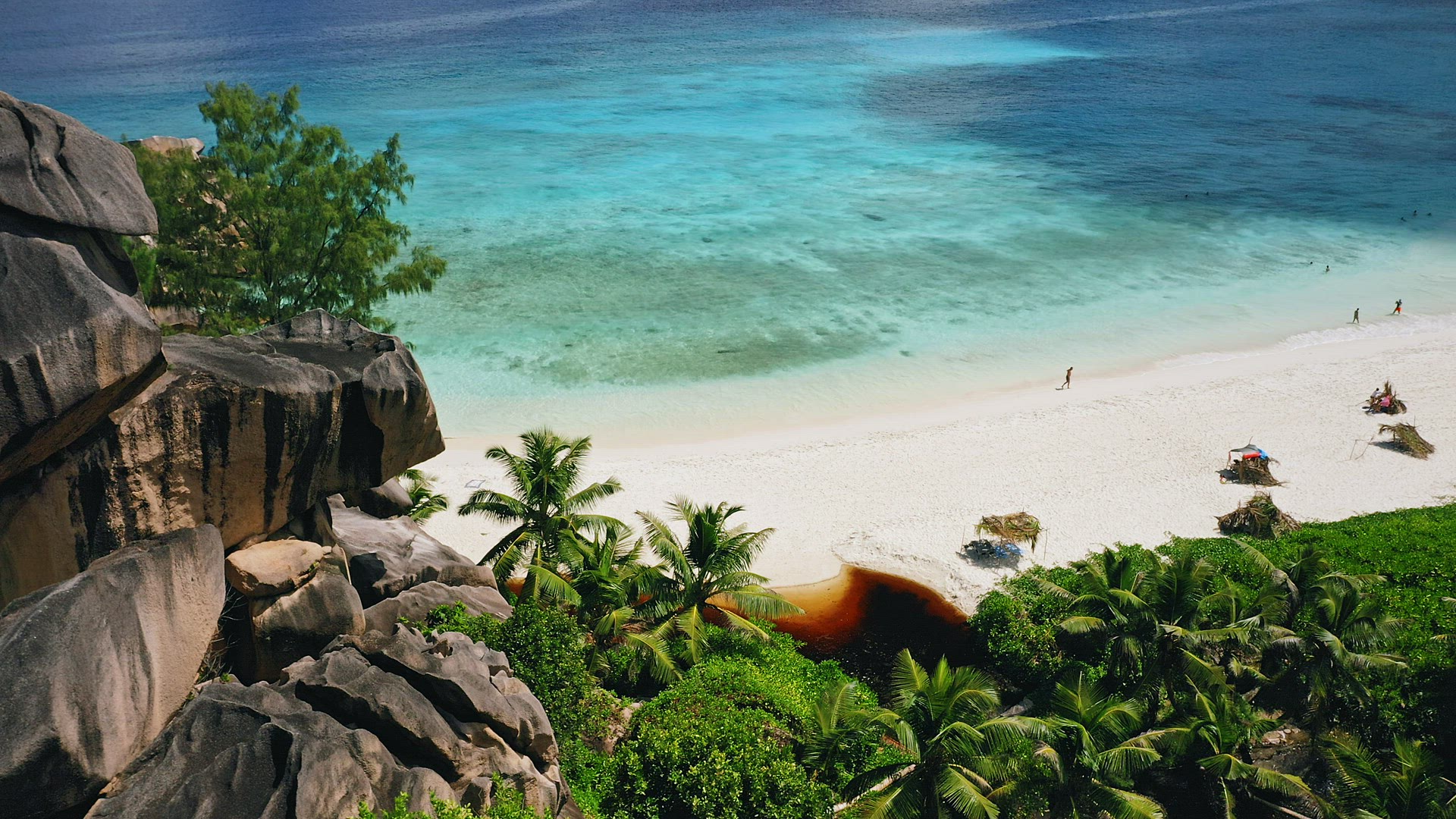 Aerial ocean reveal footage of Grand Anse beach. Crystal clear turquoise blue ocean lagoon. La Digue