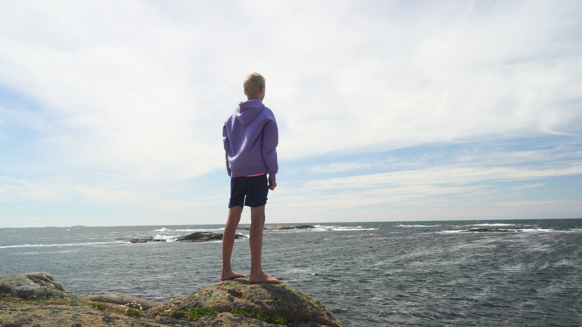 boy standing on cliff in strong wind - doing sign with arms