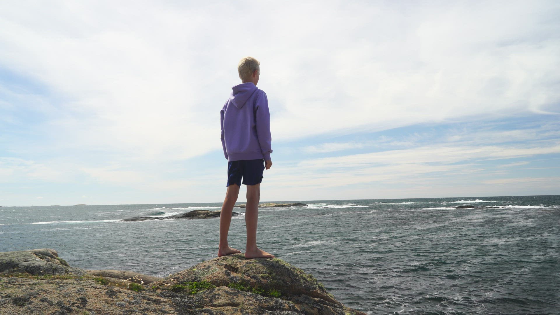 boy standing on cliff - making sign with arms - swedish west coast
