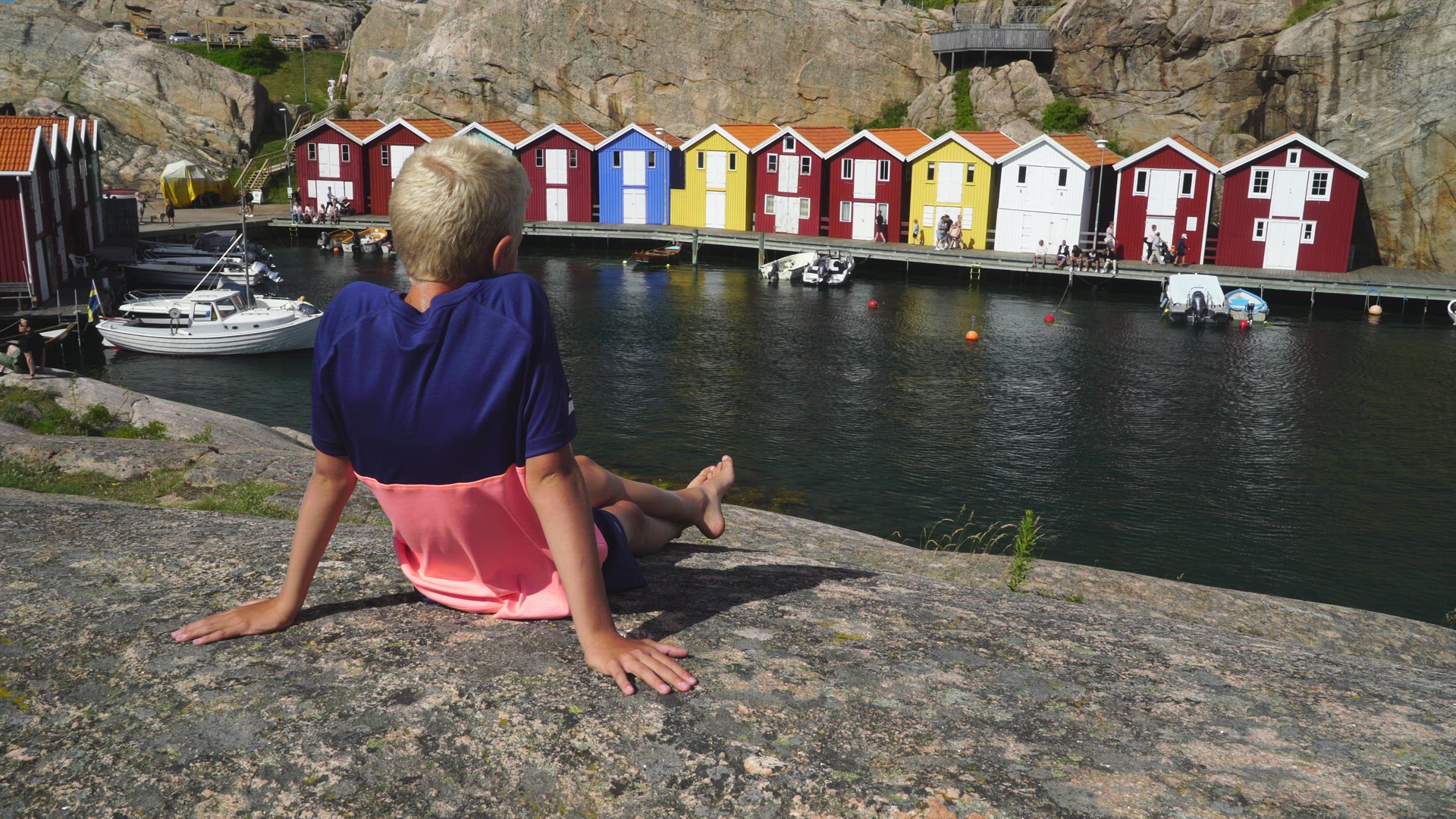 boy sitting on cliff - looking down on colourful fishinghuts on jetty in Smögen - landmarks Bohuslän