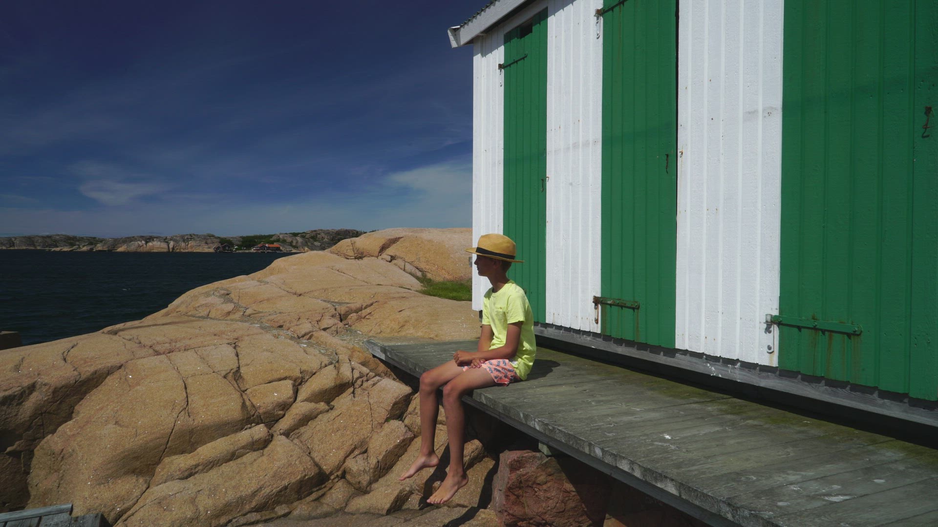 Boy with har sitting on jetty close to sea - colourful huts - seagull flying